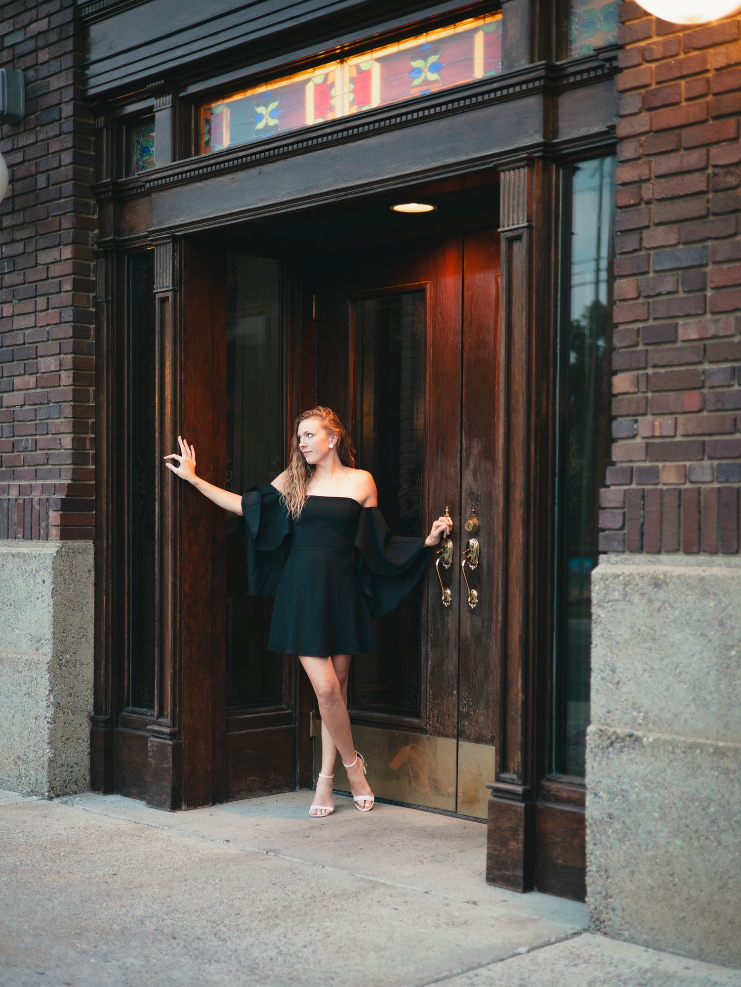 A woman in a black dress poses playfully in front of a brick building entrance. photo, Great Falls, MT