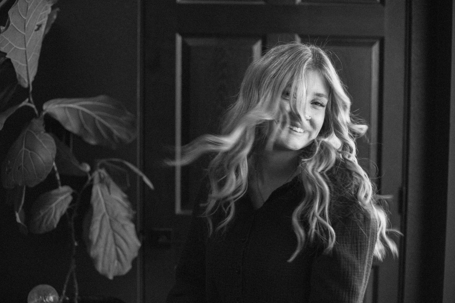 Black and white portrait of a woman with flowing blonde hair smiling against a dark background.