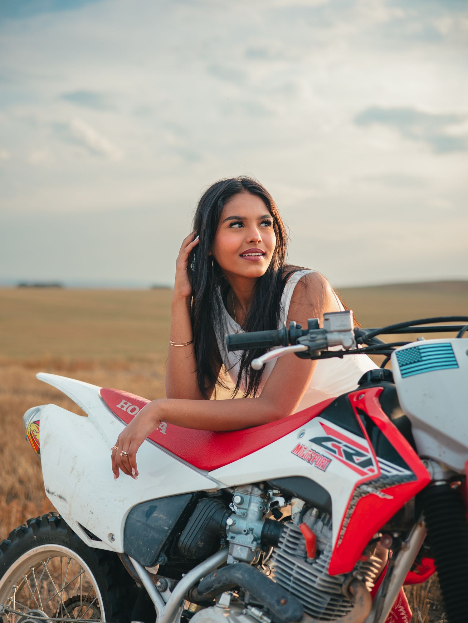 A senior leans on a red and white dirt bike in a desert landscape during golden hour. photo, Great Falls, MT