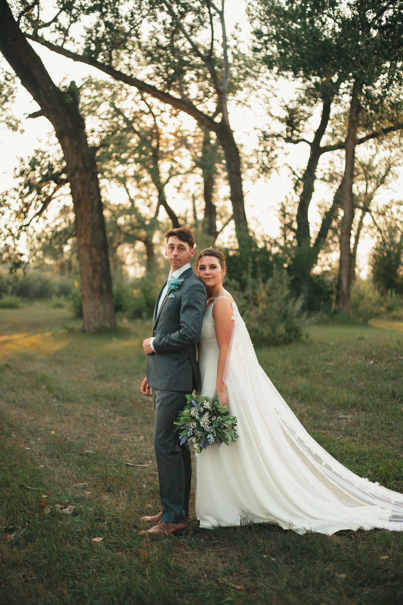 A romantic outdoor wedding photo session among tall trees at sunset with flowing white gown and greenery. Great Falls, Montana
