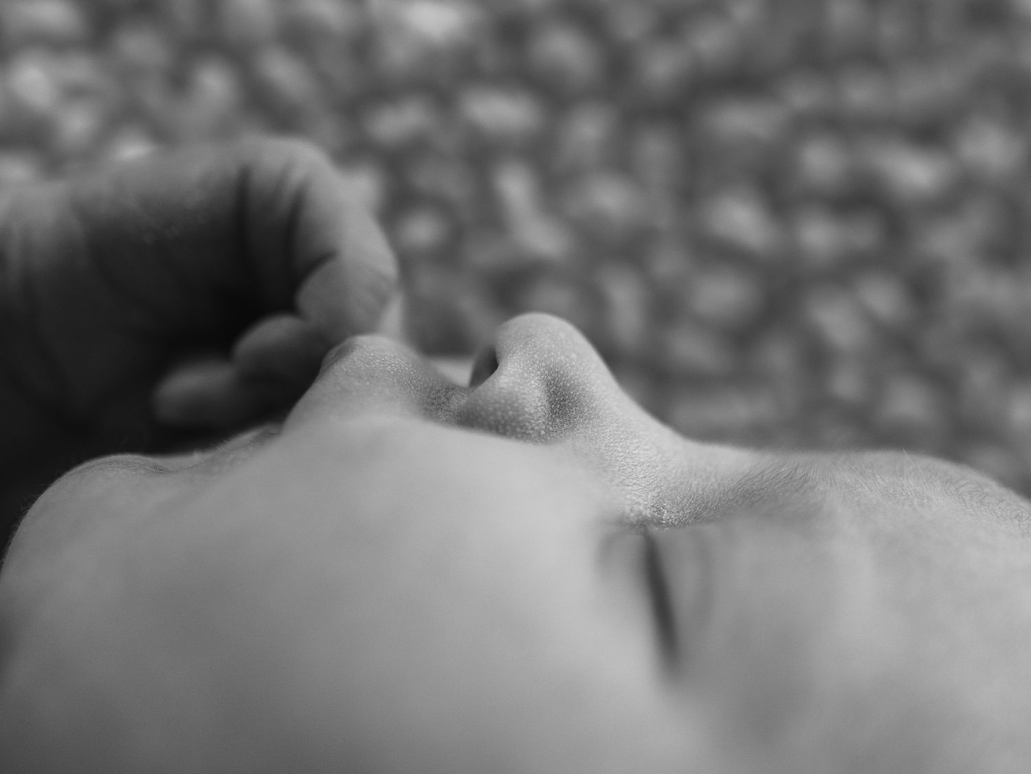 Black and white close-up photo of a sleeping baby's face with a hand gently resting nearby.