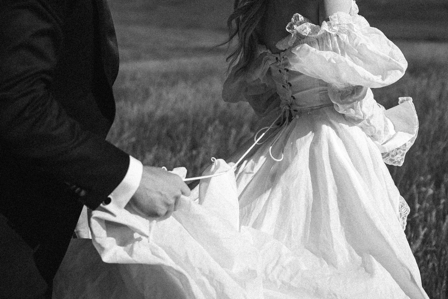 Black and white photo of bride in vintage lace wedding gown held by groom in suit outdoors.