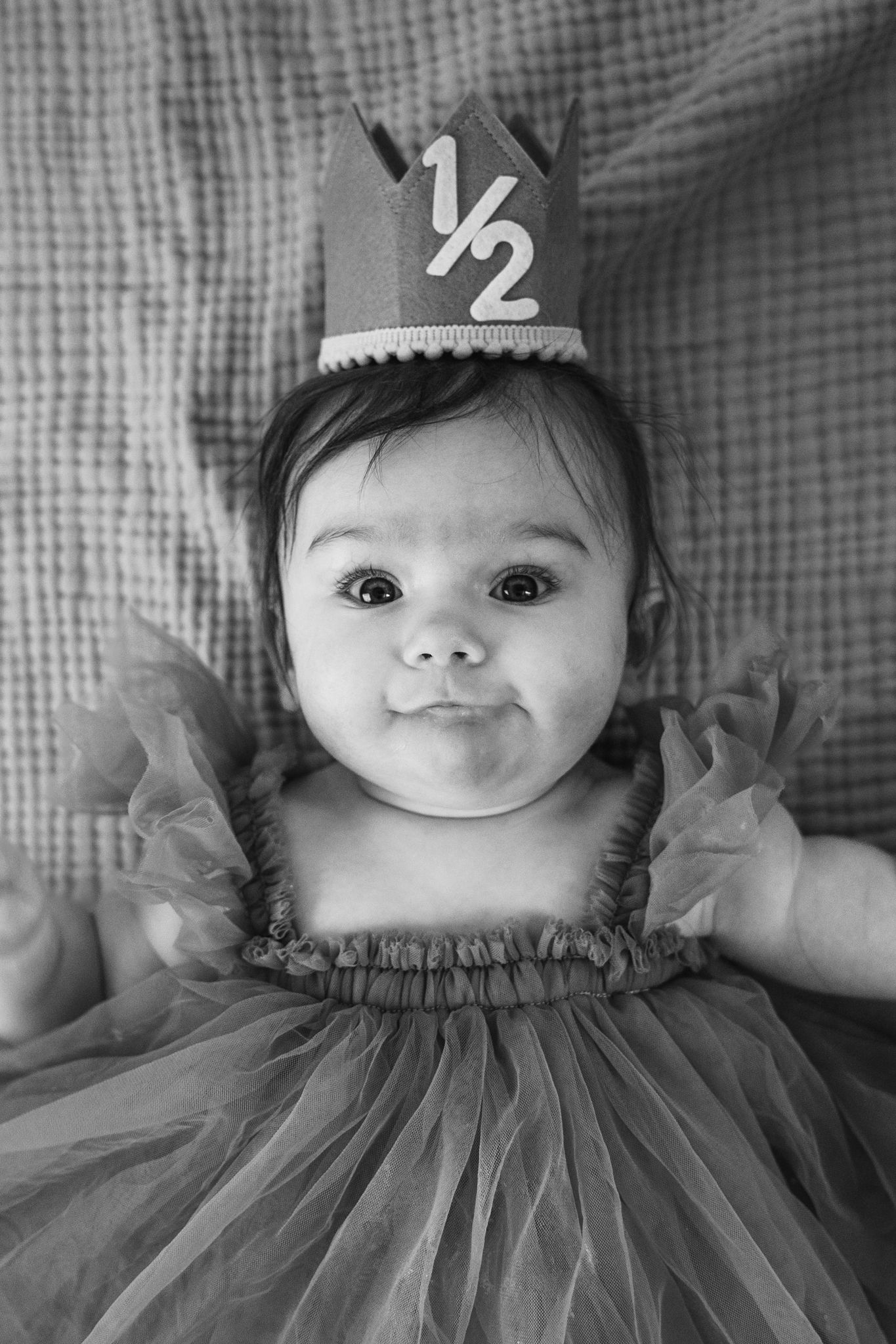 Black and white photo of a cute baby girl wearing a half birthday crown and tutu dress, celebrating her 6-month milestone.