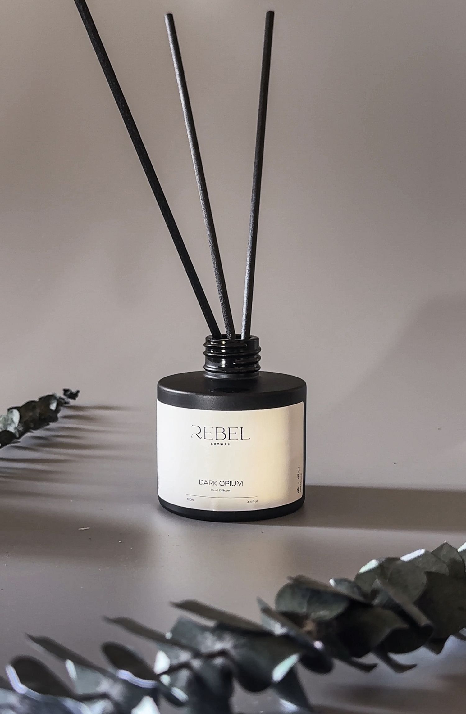 Black reed diffuser sticks arranged in a sleek glass container casting dramatic shadows against a light gray background.