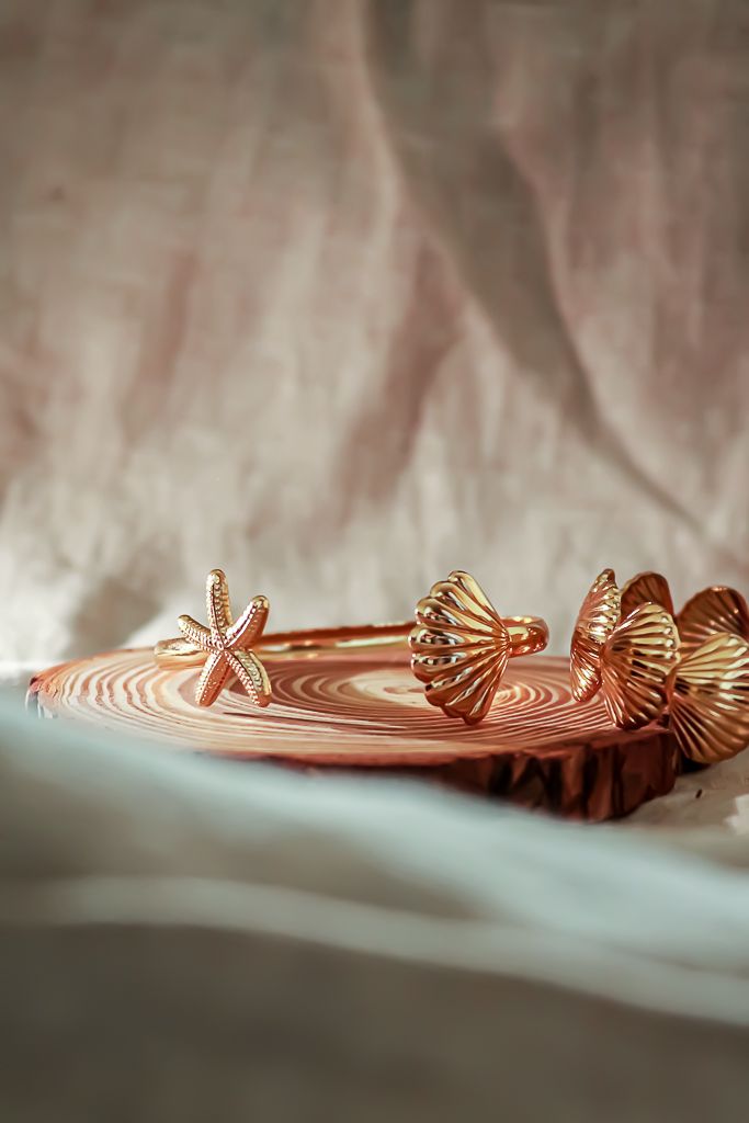 Rose gold seashell and starfish hair accessories arranged on a textured surface with dramatic lighting.