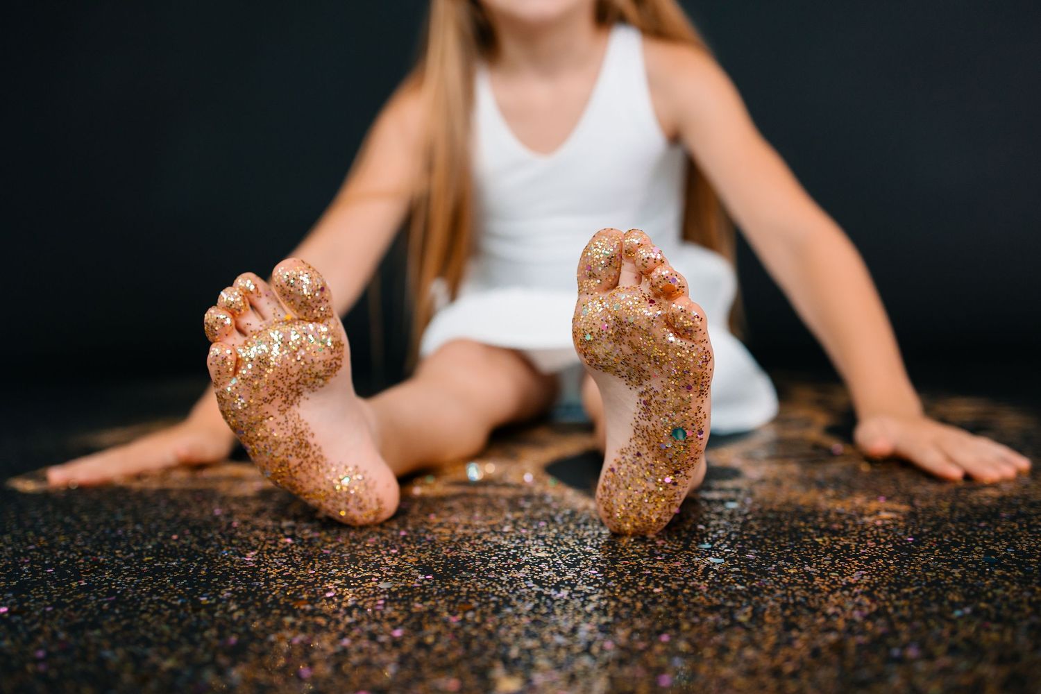 A little girl with her feet covered in golden glitter and sparkles.