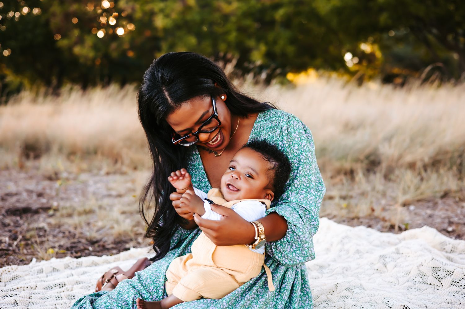 A mother with her son in her lap. Together they are lying in a grassy field during a sunset photoshoot on a blanket.