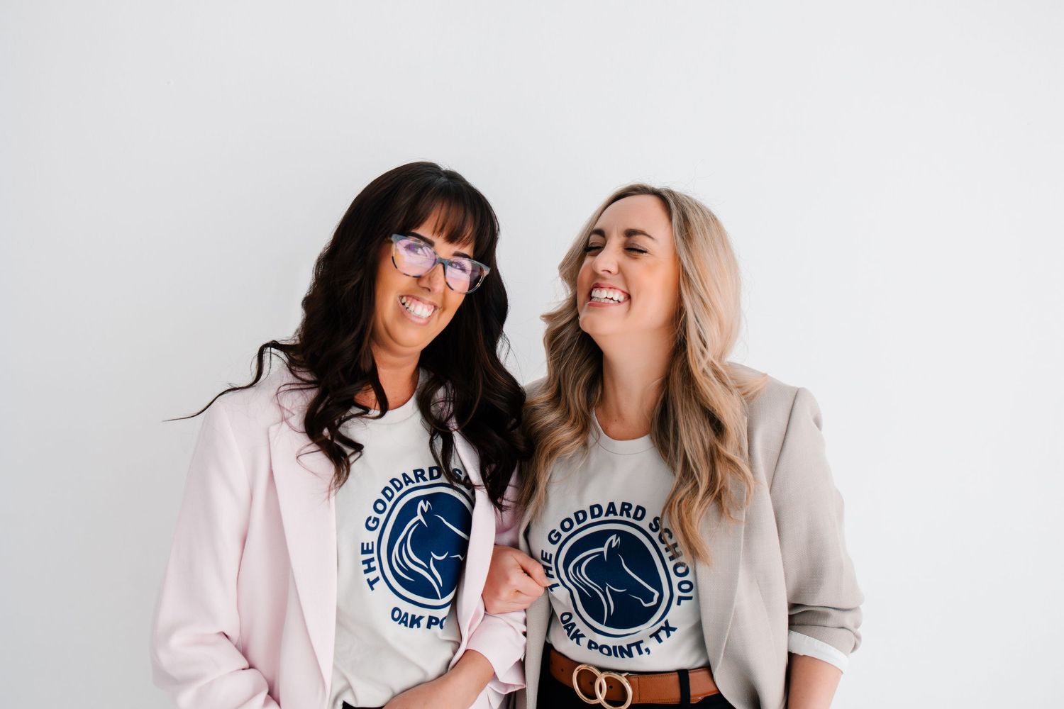 Two women wearing matching graphic business t-shirts laugh together against a white background.