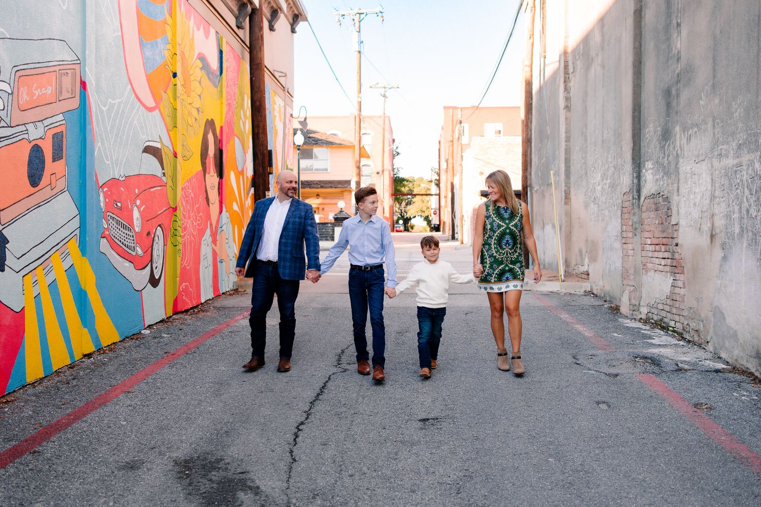 People walking down an urban alley with colorful geometric murals painted on concrete walls.
