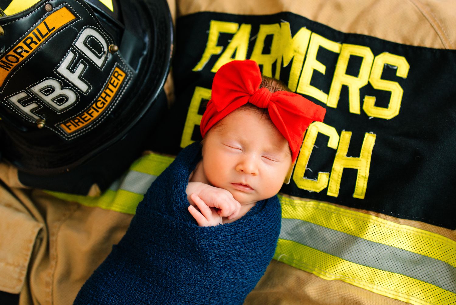 A newborn daughter against her father's firefighter gear and hat.