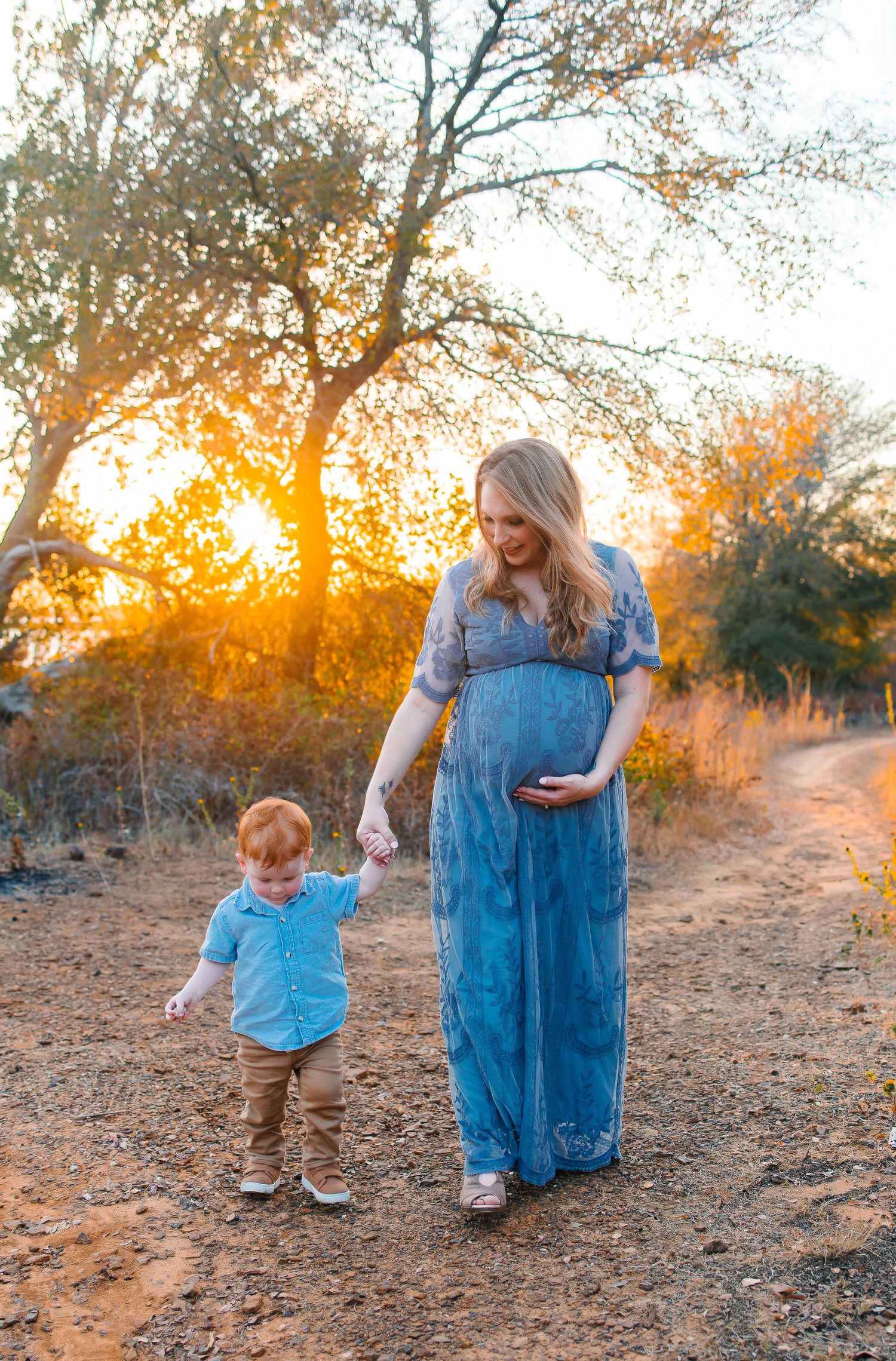 A mother and her son walk together on a dusty path at sunset while wearing matching denim and blue outfits.