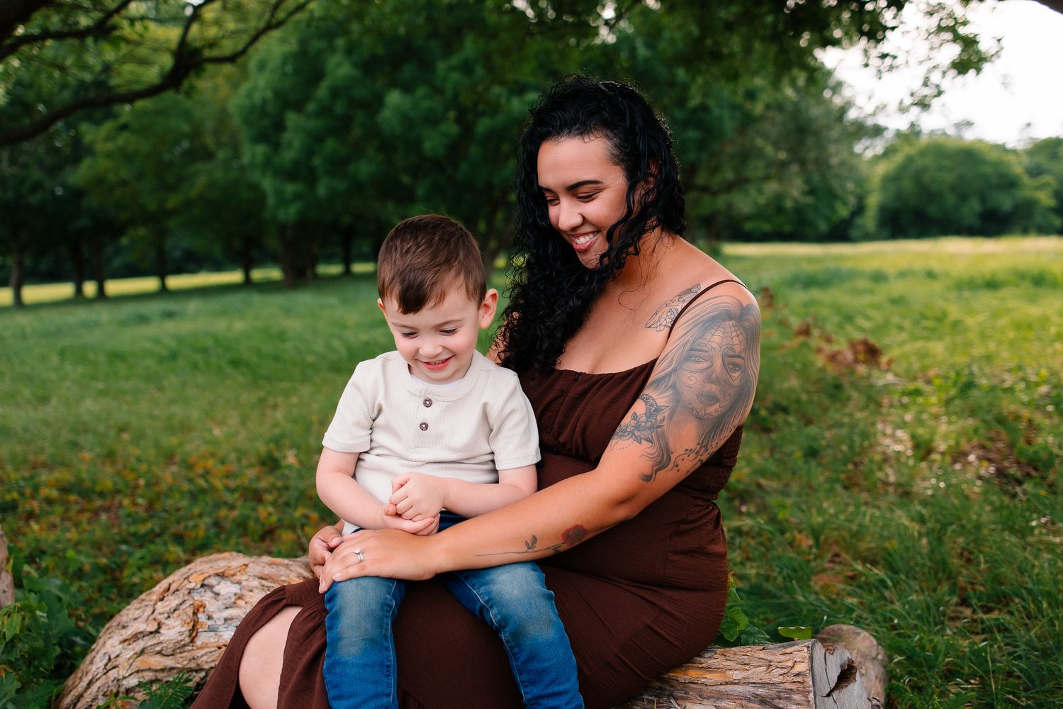 A parent and child share playful moments together while sitting on tree logs in a lush green meadow.