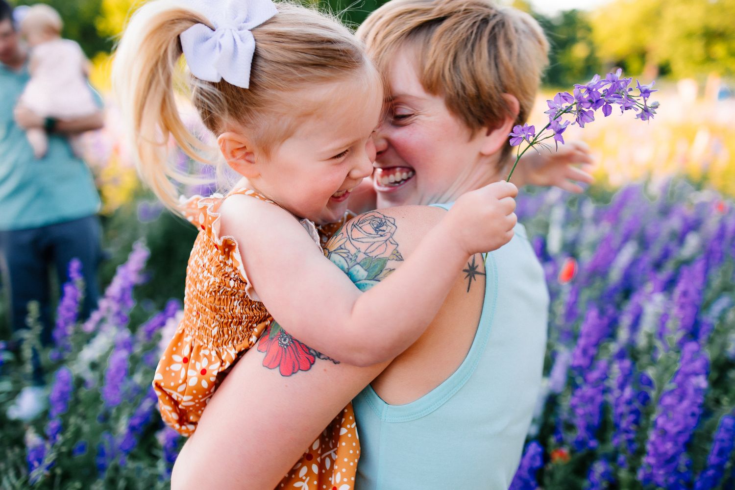 Two people share a tender moment in a colorful garden filled with purple lupines and golden evening light.