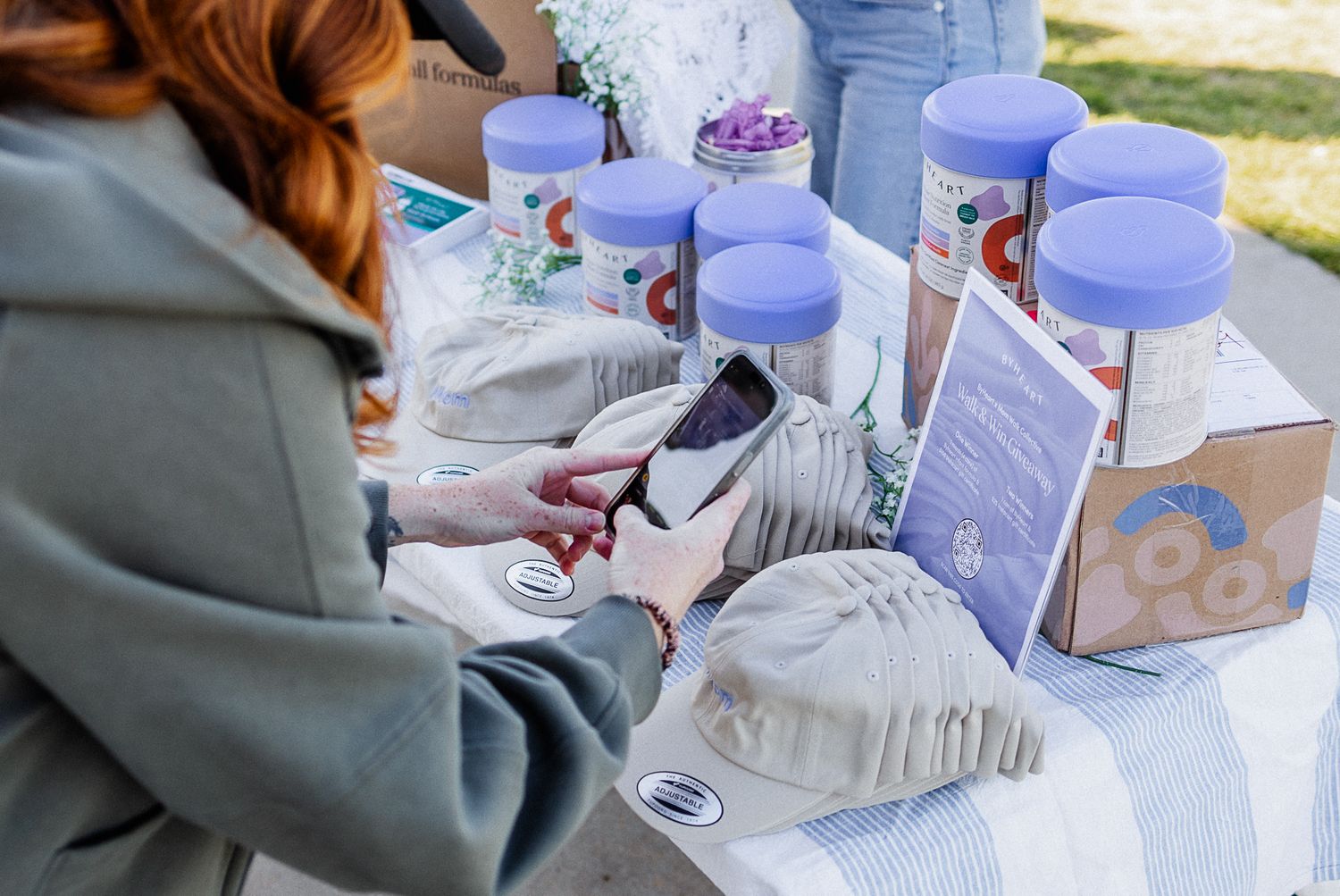 Someone capturing a code with her phone camera at an event with purple jars and decorative items on a table outdoors.