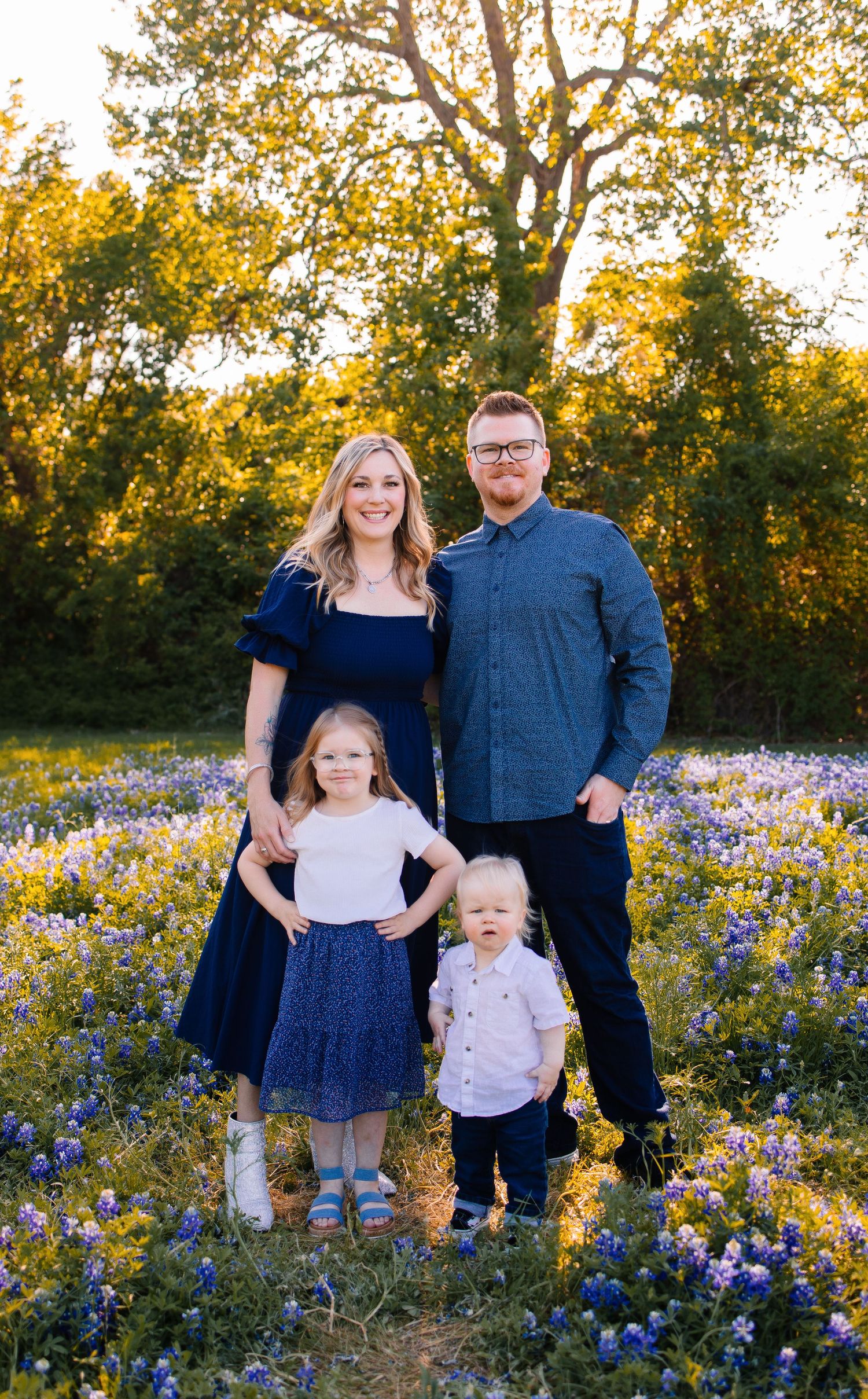 A family poses together in a field of vibrant bluebonnets during golden hour sunset.