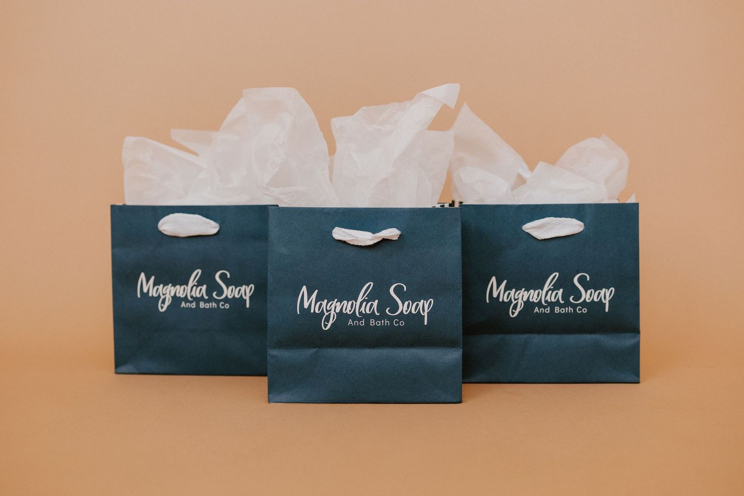 Navy blue tissue boxes arranged in a row against a beige background showing Magnolia Soap branding and packaging design.