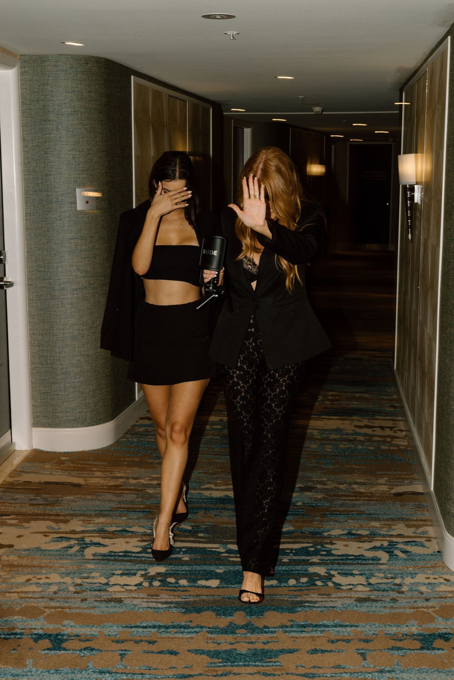 People walking and posing playfully in a hotel corridor with decorative blue carpeting.