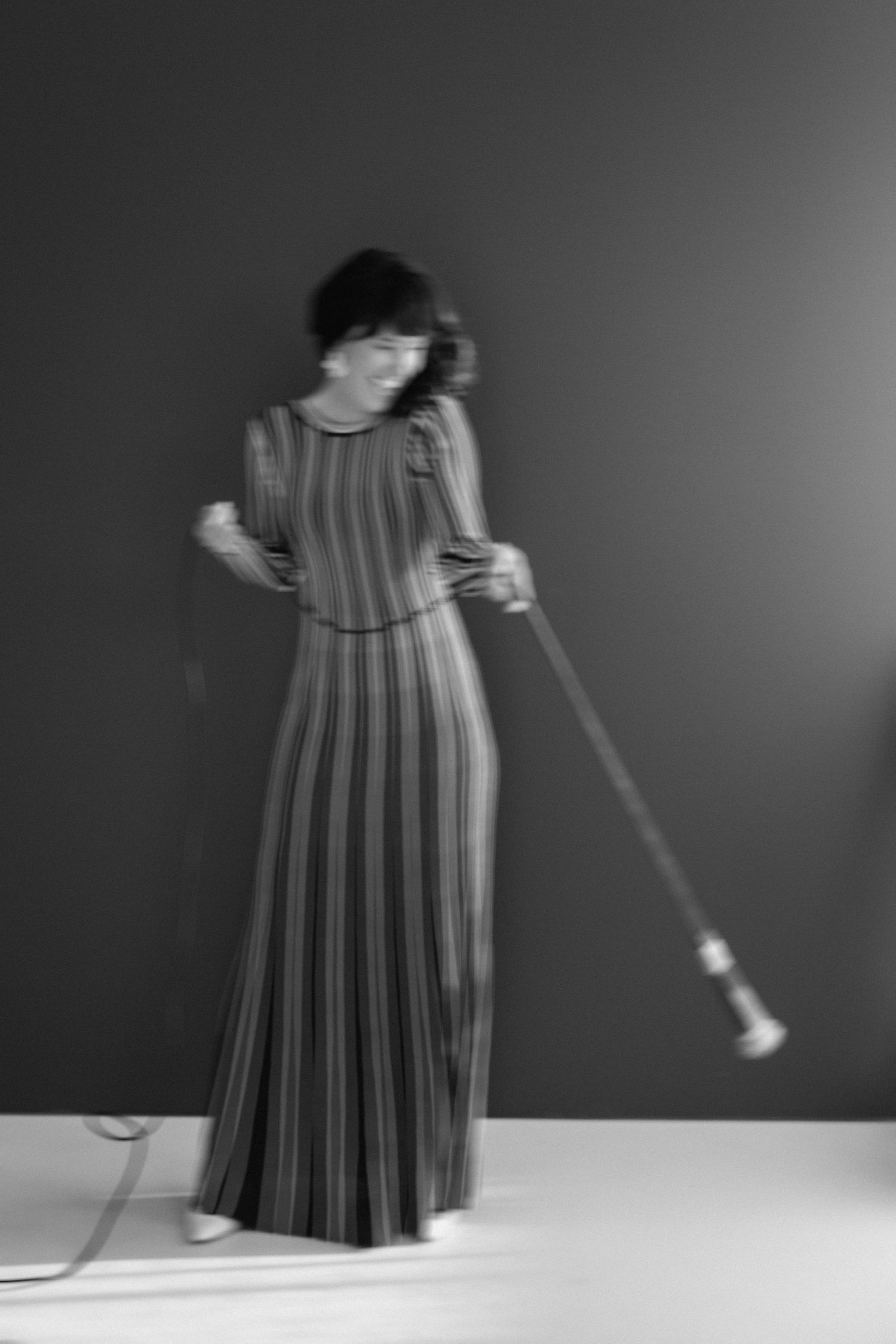 A black and white sequence shows a pleated dress swaying in motion against a dark background.