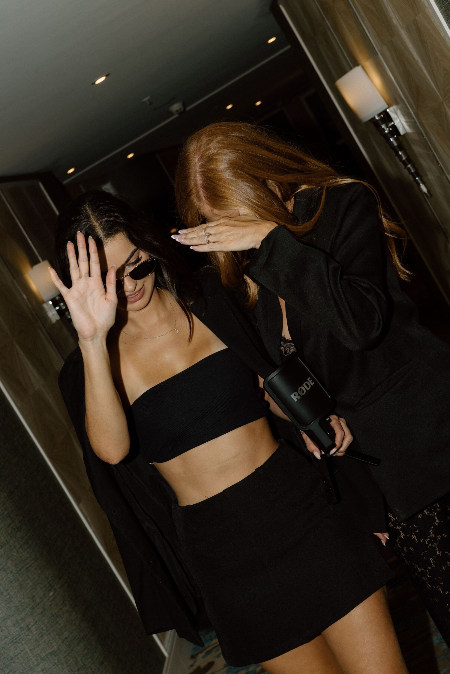 Group walking in dark clothing through hallway with hands raised to block camera.