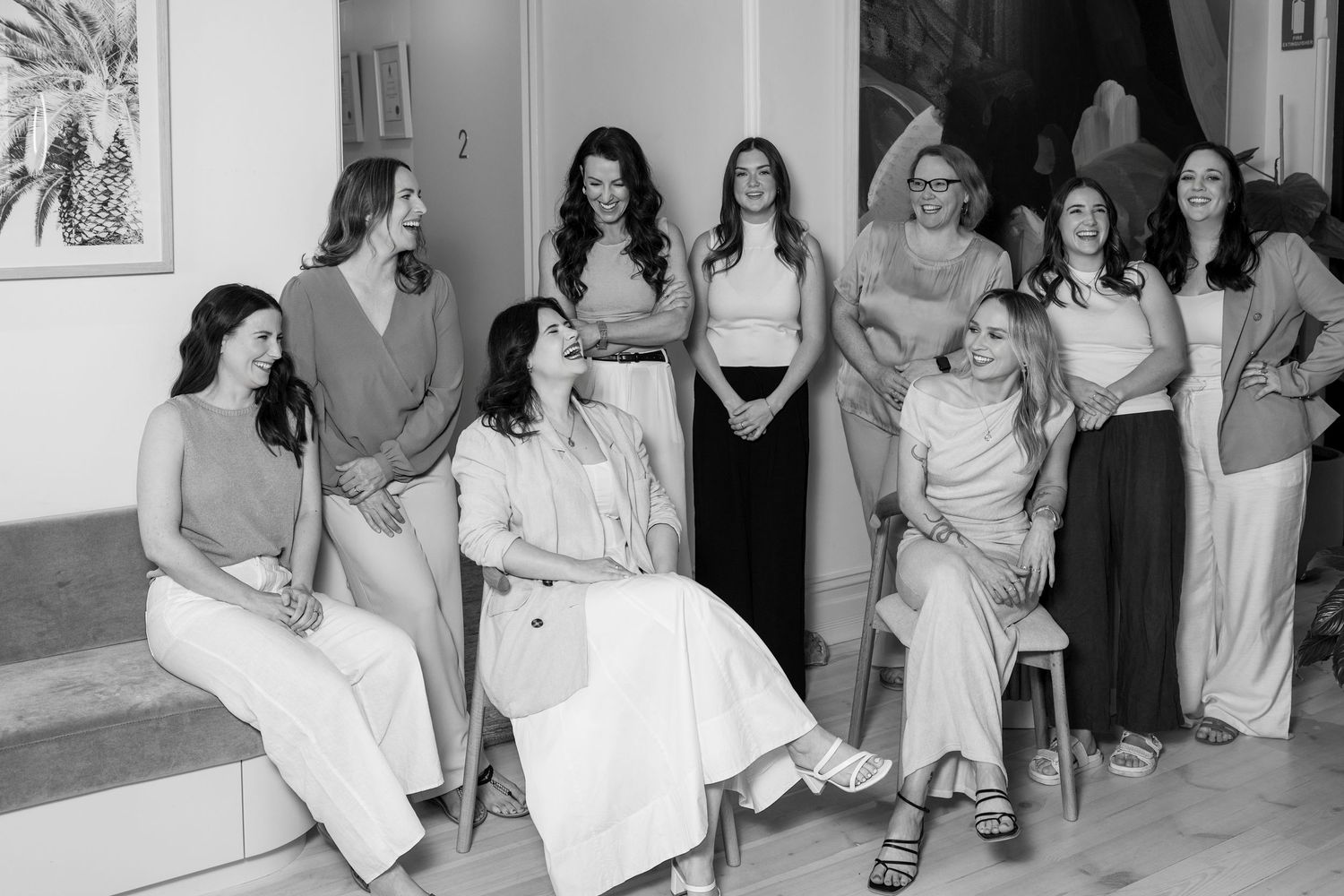 Black and white photo of a group of women smiling and posing together indoors at a bright, elegant venue.