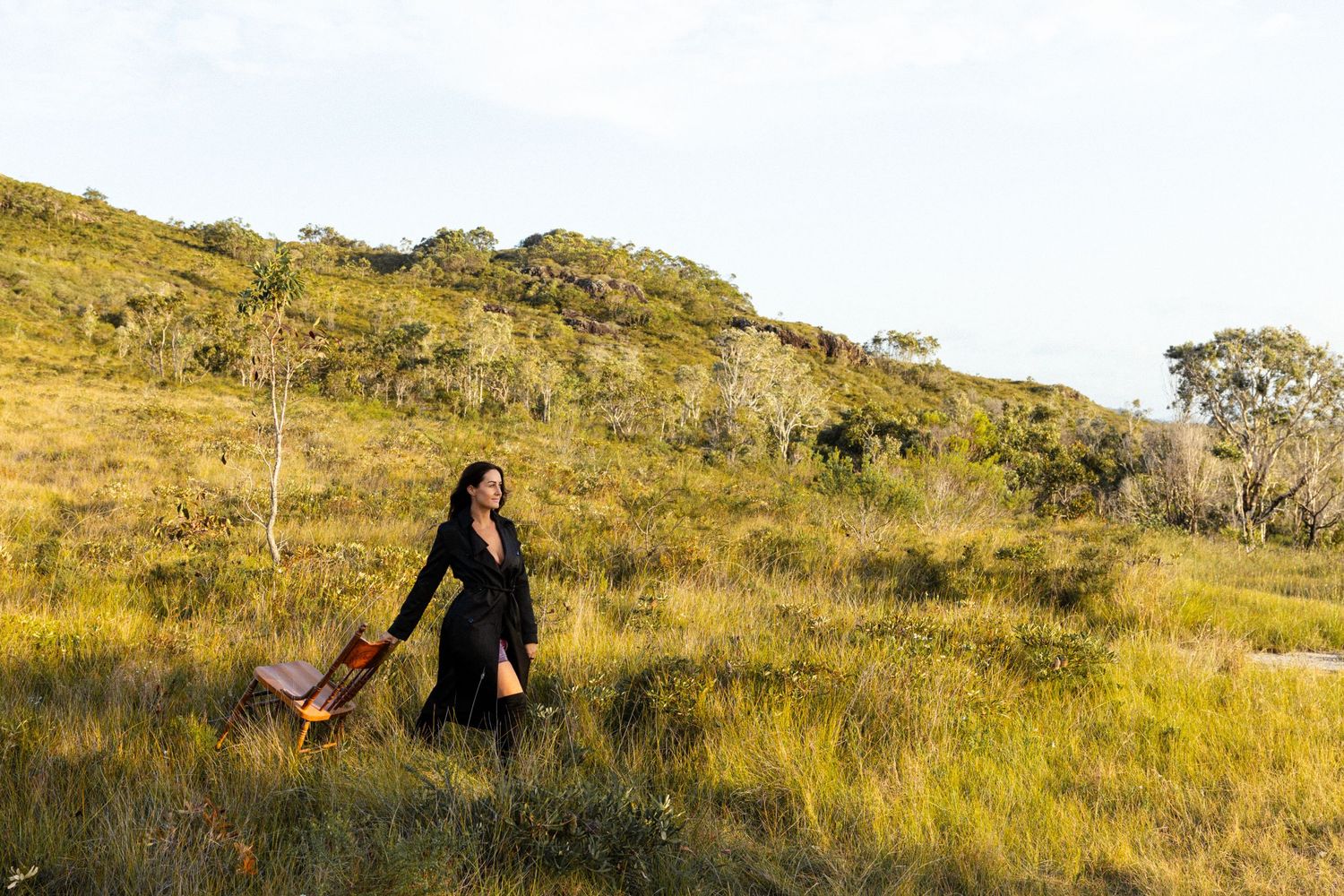 Silhouette of person with chair on hilltop during golden hour.