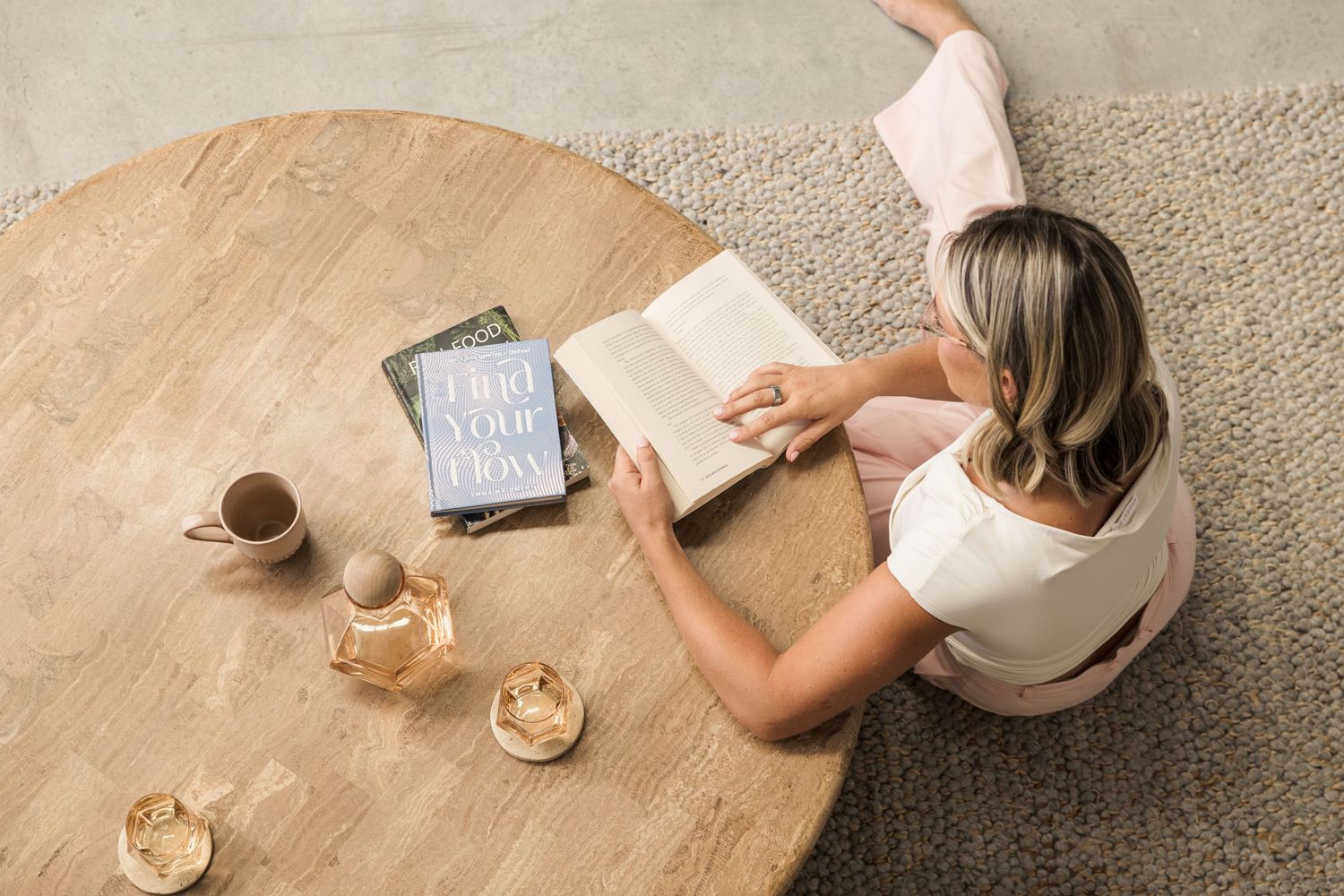 Overhead view of hands reaching for coffee and books on wooden table.