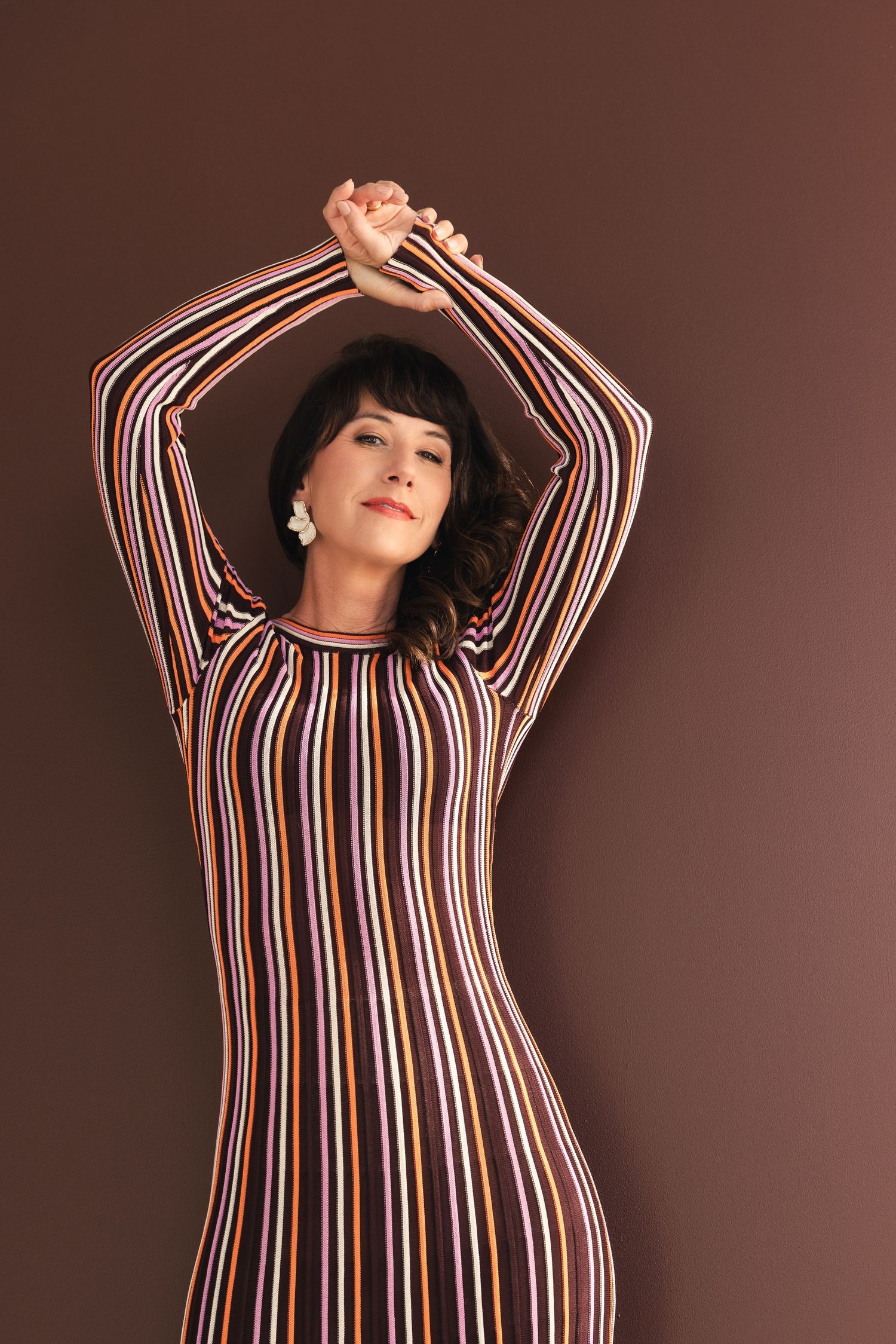 Fashion poses in striped dress against brown studio backdrop.