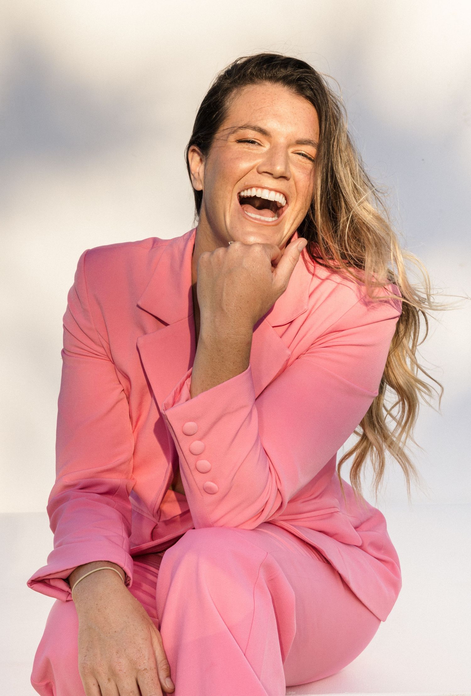 A person in a pink blazer laughs joyfully while posing against a light background in a series of candid shots.