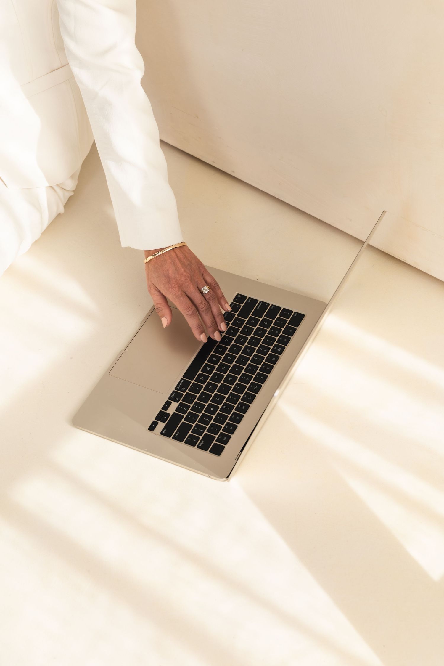 Hands type on a silver laptop keyboard against a white minimalist background with dramatic shadows.