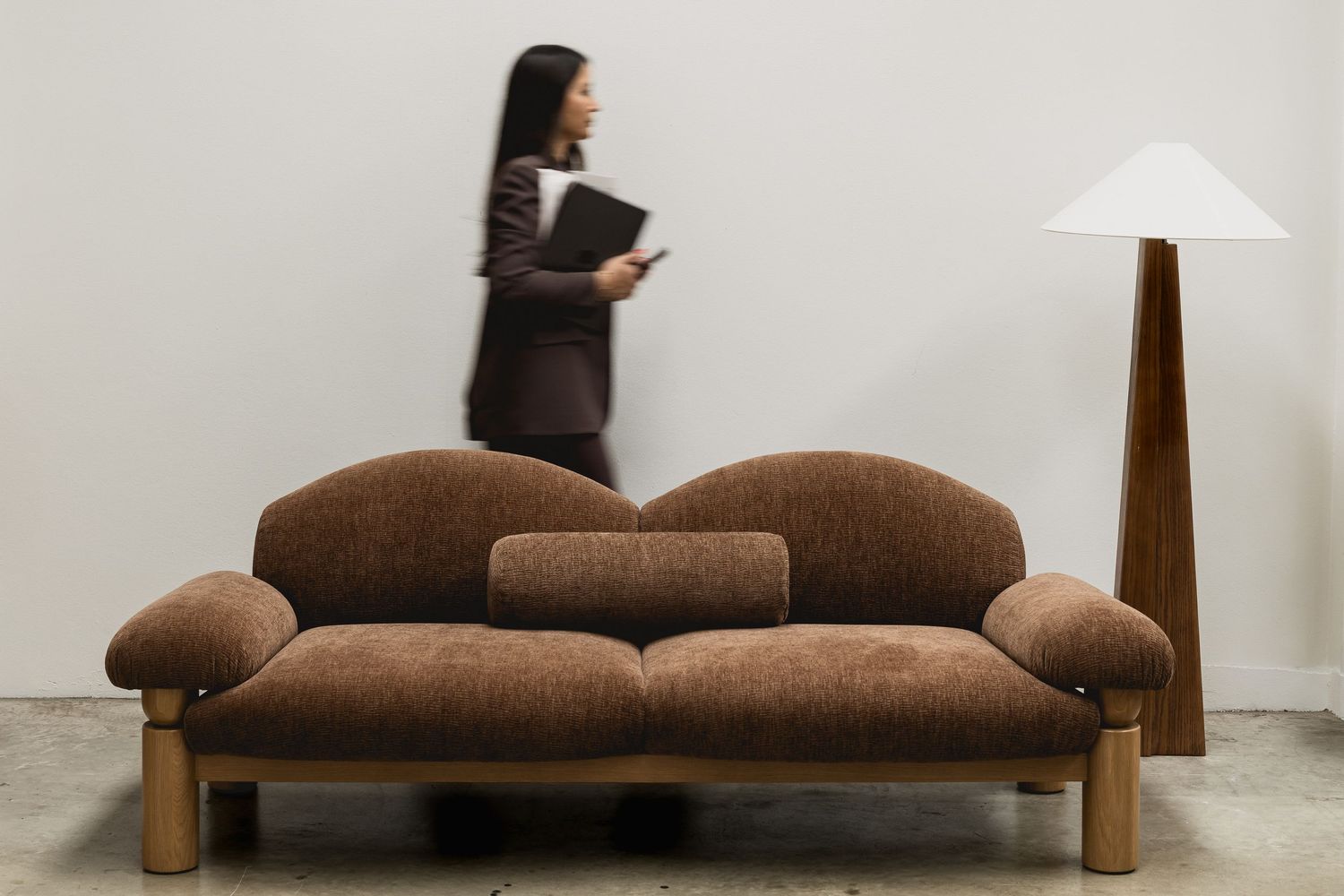 A brown upholstered sofa shown from multiple angles in a minimalist gallery-like setting against white walls.