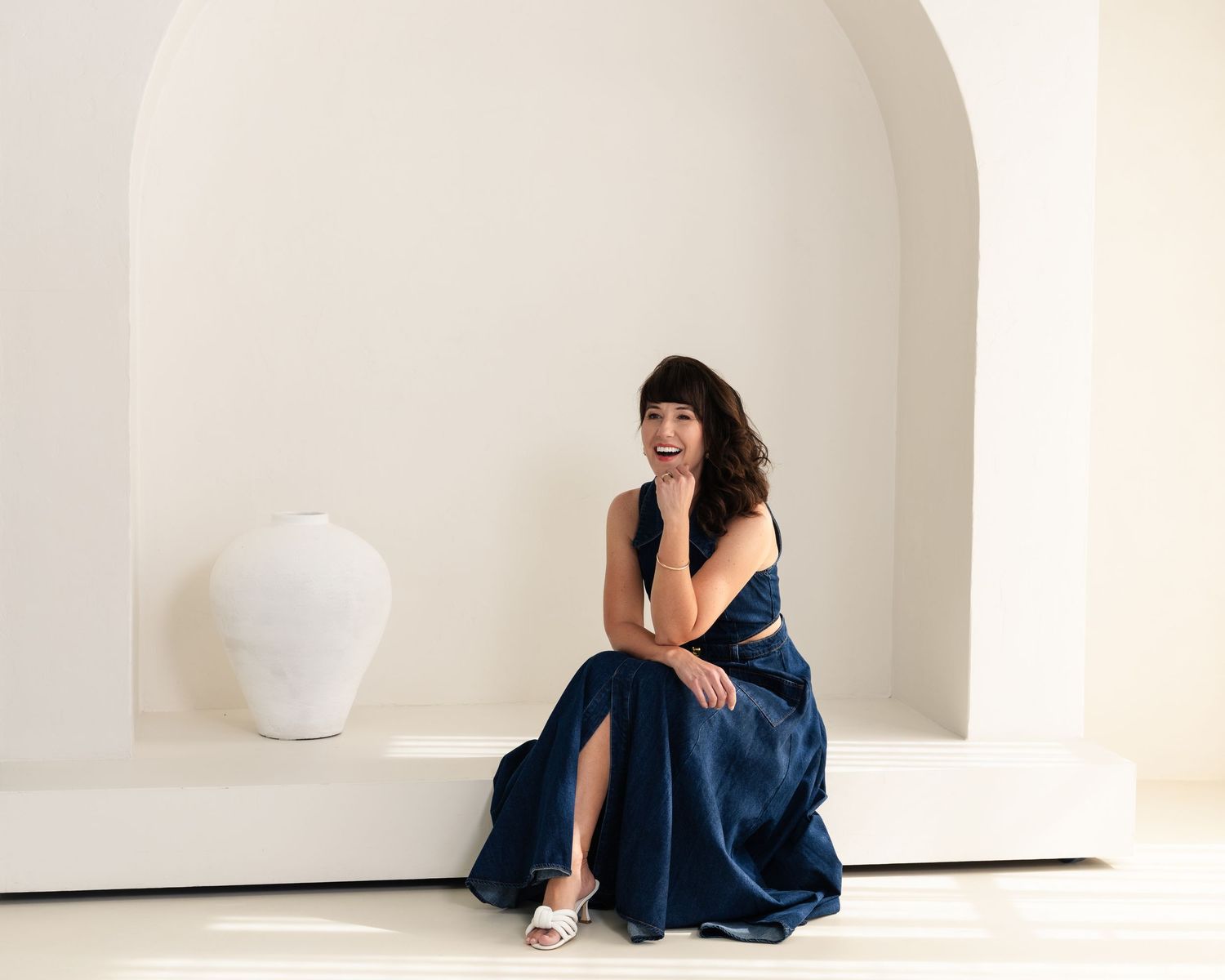 A navy dress is photographed in an artistic series against a minimalist white curved wall.