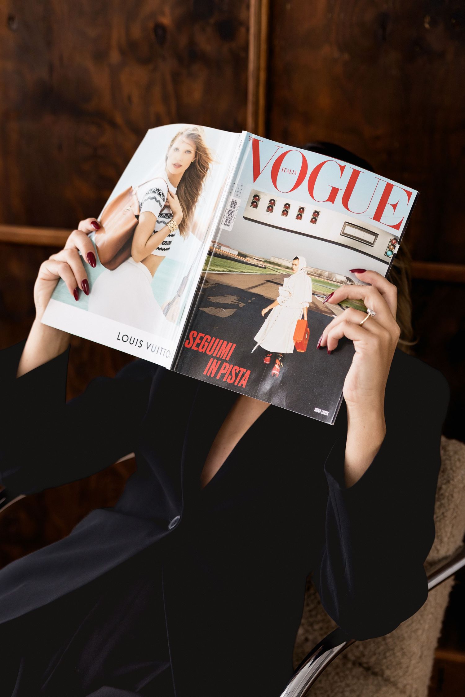 A person in black clothing lies down while reading a fashion magazine in a relaxed position.