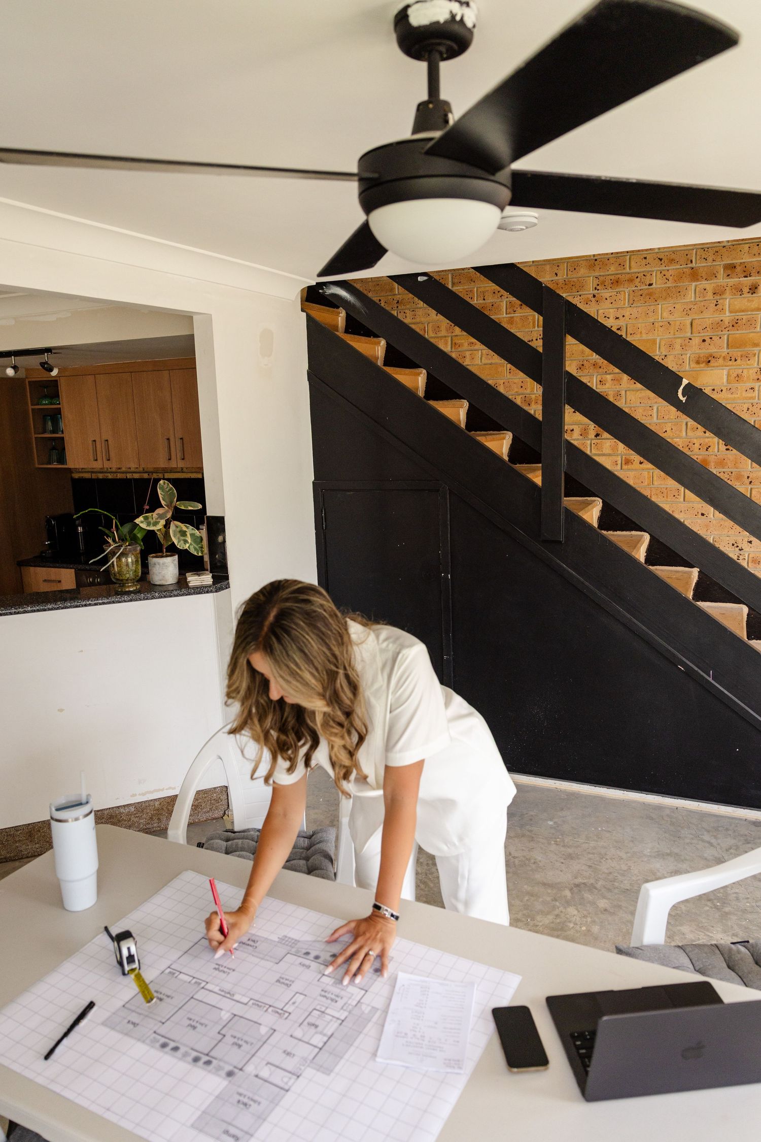 Woman in white outfit reviews architectural blueprints on a table in a modern home interior.