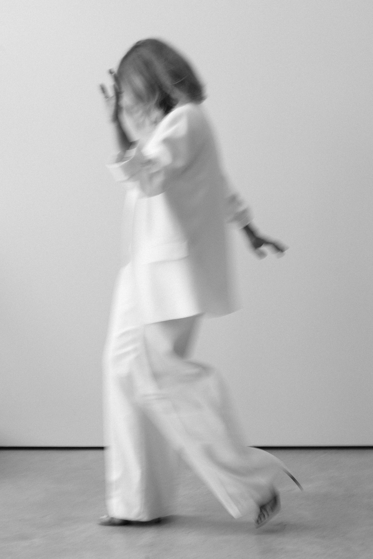 Blurred black and white photo of a woman in a white suit walking dynamically, creating a motion blur effect.