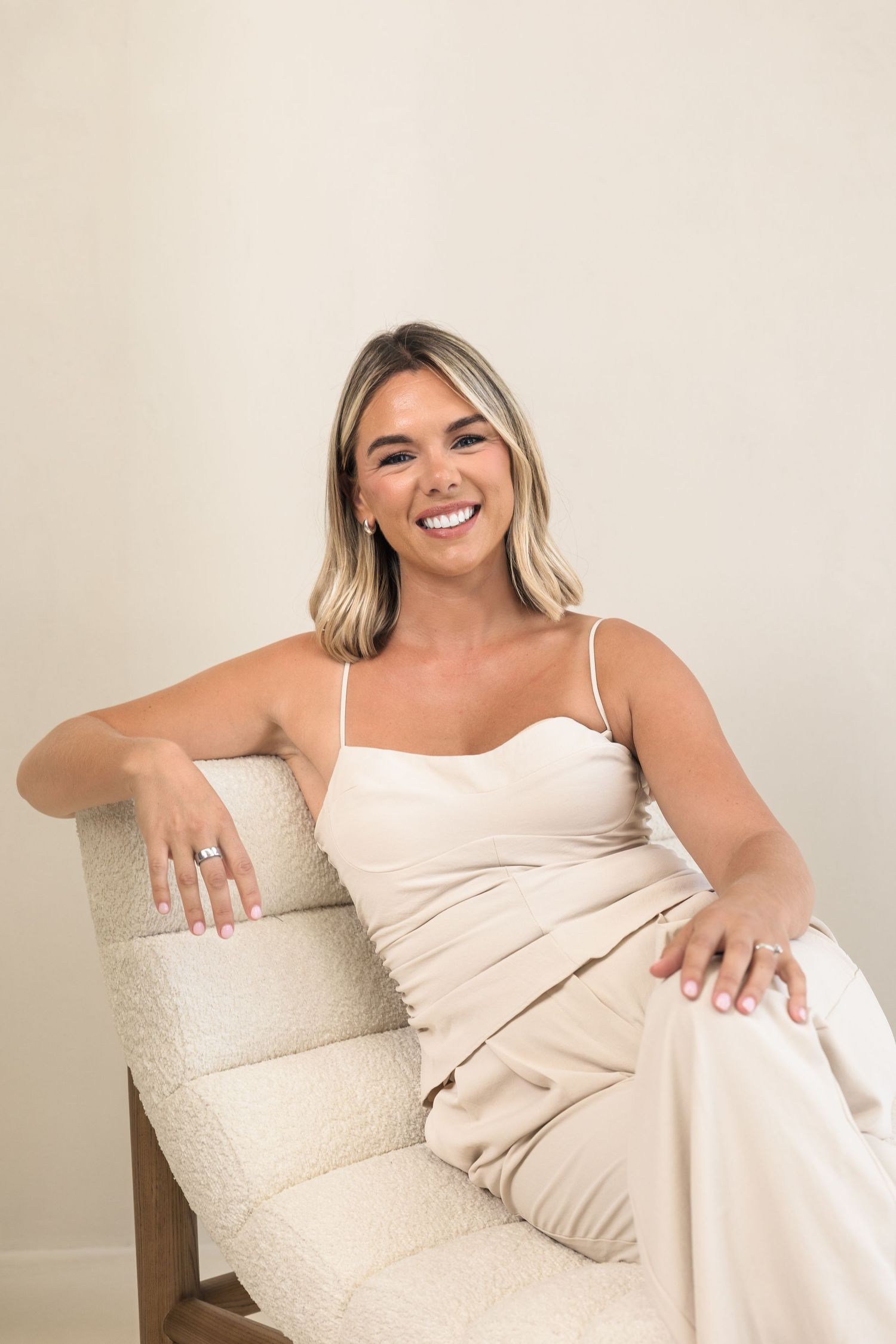 Woman in white dress lounging on beige couch in casual lifestyle photoshoot.