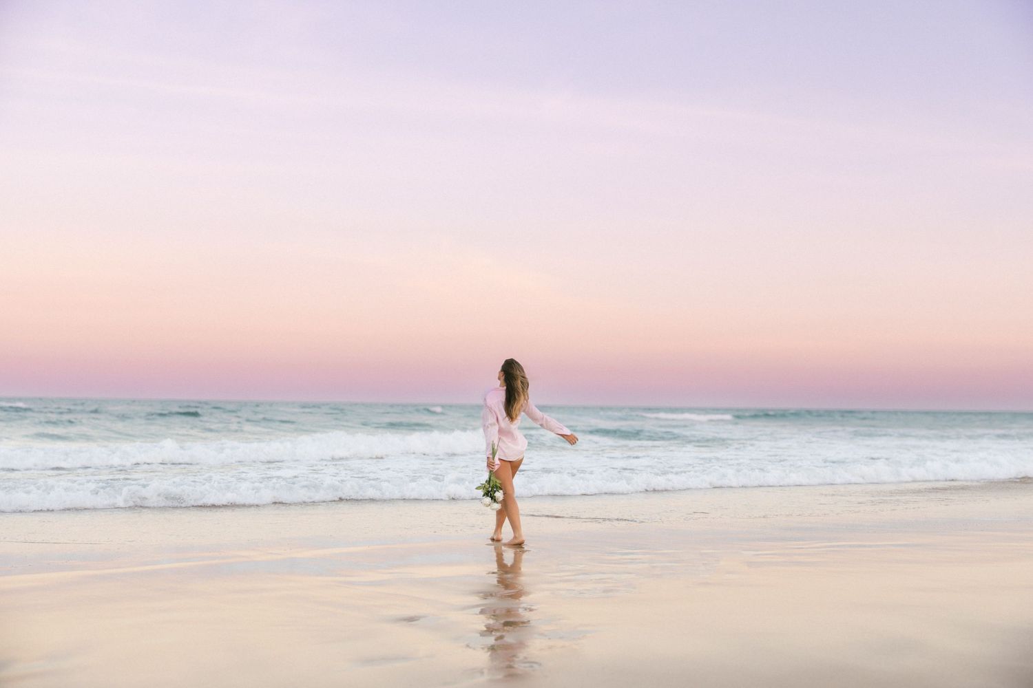 A dreamy beach scene at dusk with a figure walking along the shoreline in pastel lighting.