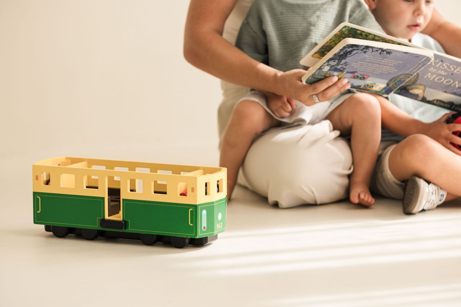 Child playing with vintage toy trains on white floor in natural lighting.