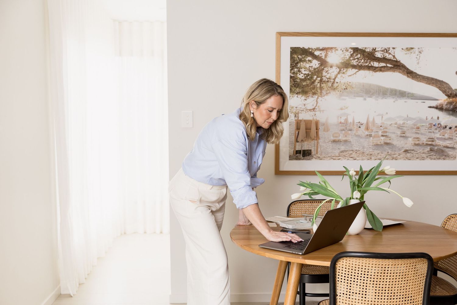Professional working at a modern home office desk with laptop and houseplant in natural light setting.
