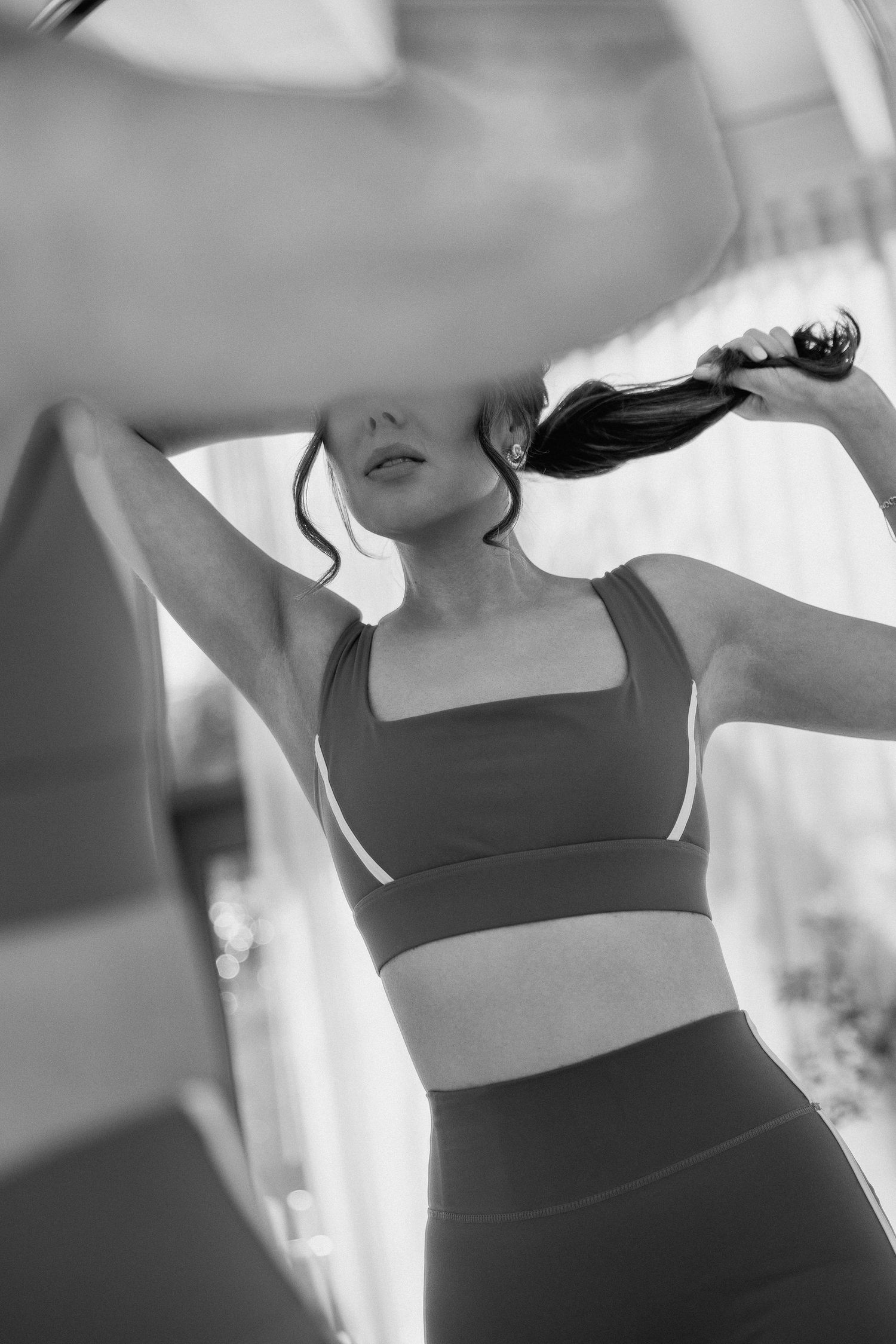 Black and white photo of a woman in a sports bra and leggings posing with her hair in a ponytail.