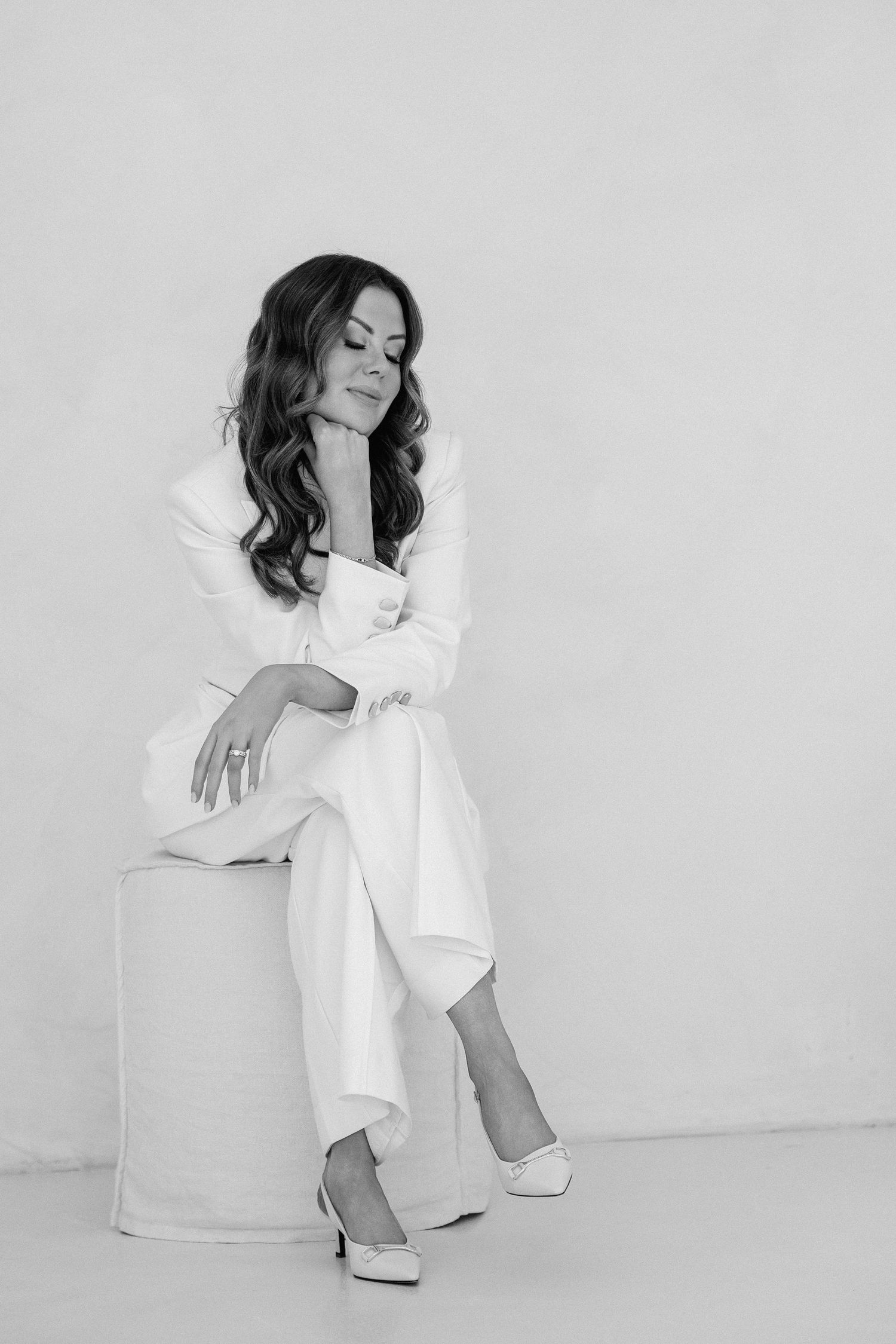 Elegant woman in white suit sitting on a pedestal, black and white fashion portrait.