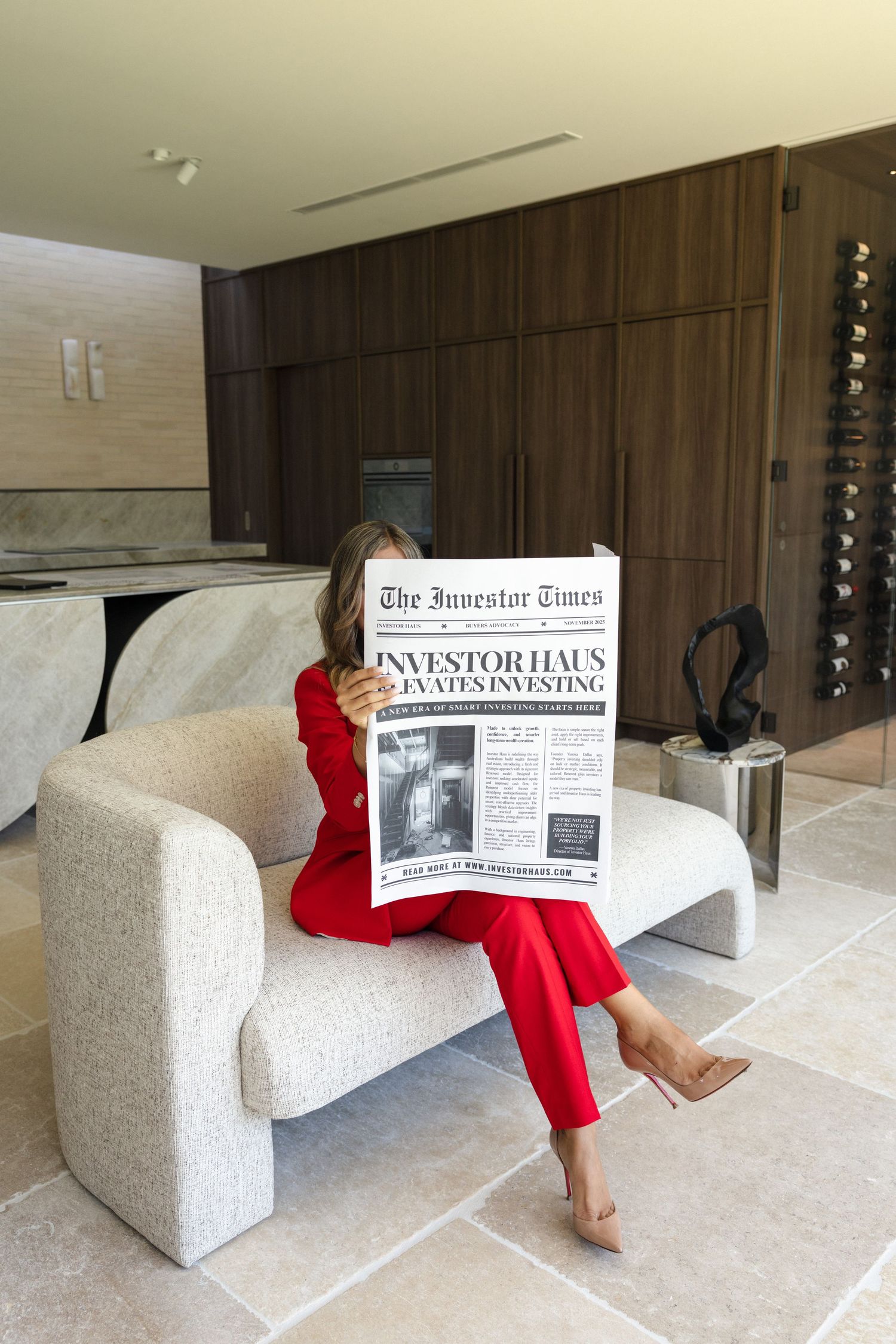 Woman in red suit reading The Investor Times newspaper while seated in a modern luxury living space.