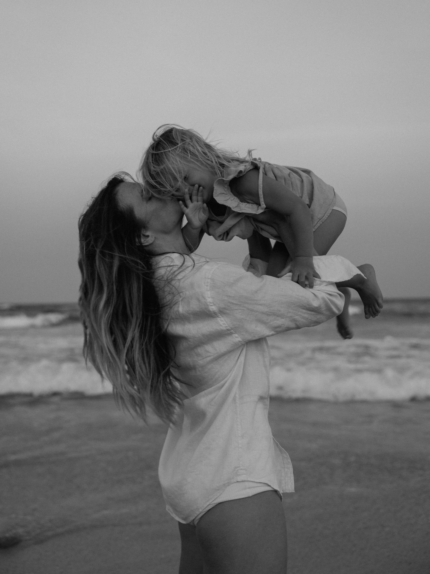 A series of black and white photos showing someone lifting and playing with a small child on a beach.