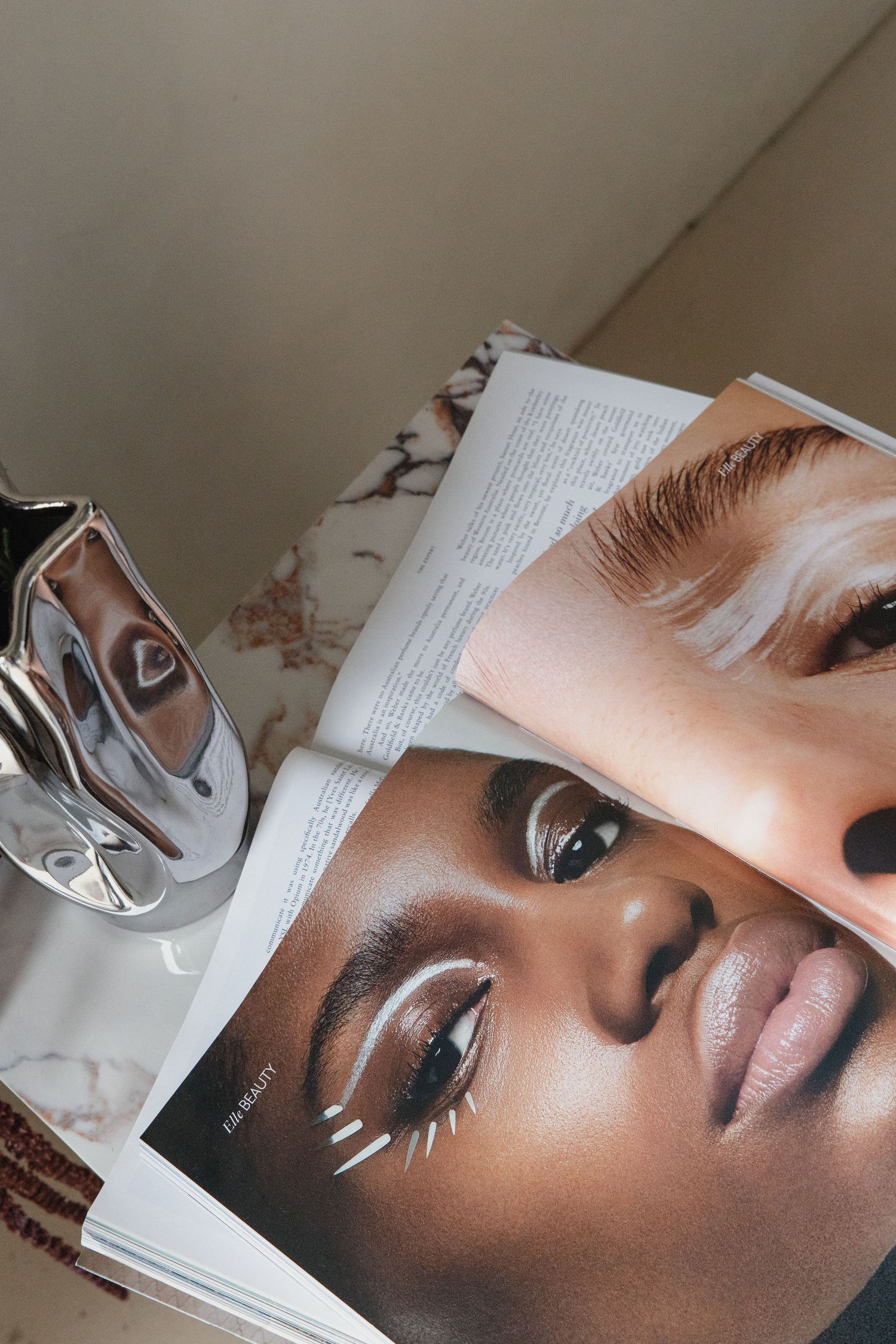 Beauty magazine pages featuring diverse models with bold eye makeup displayed on a nightstand.