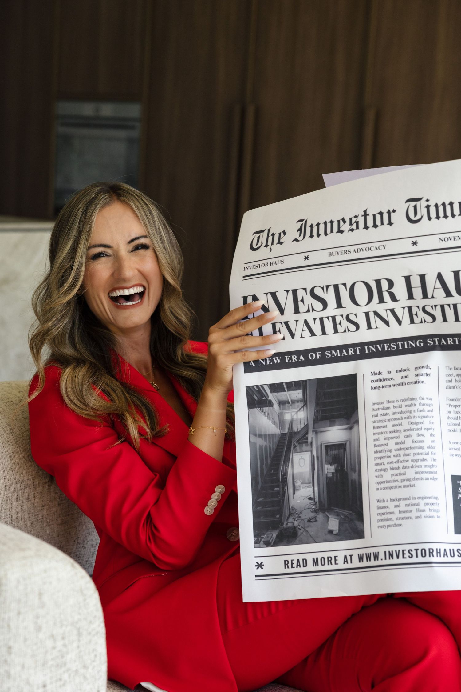 Laughing woman in red suit holds The Investor Times newspaper featuring Investor Haus headline.