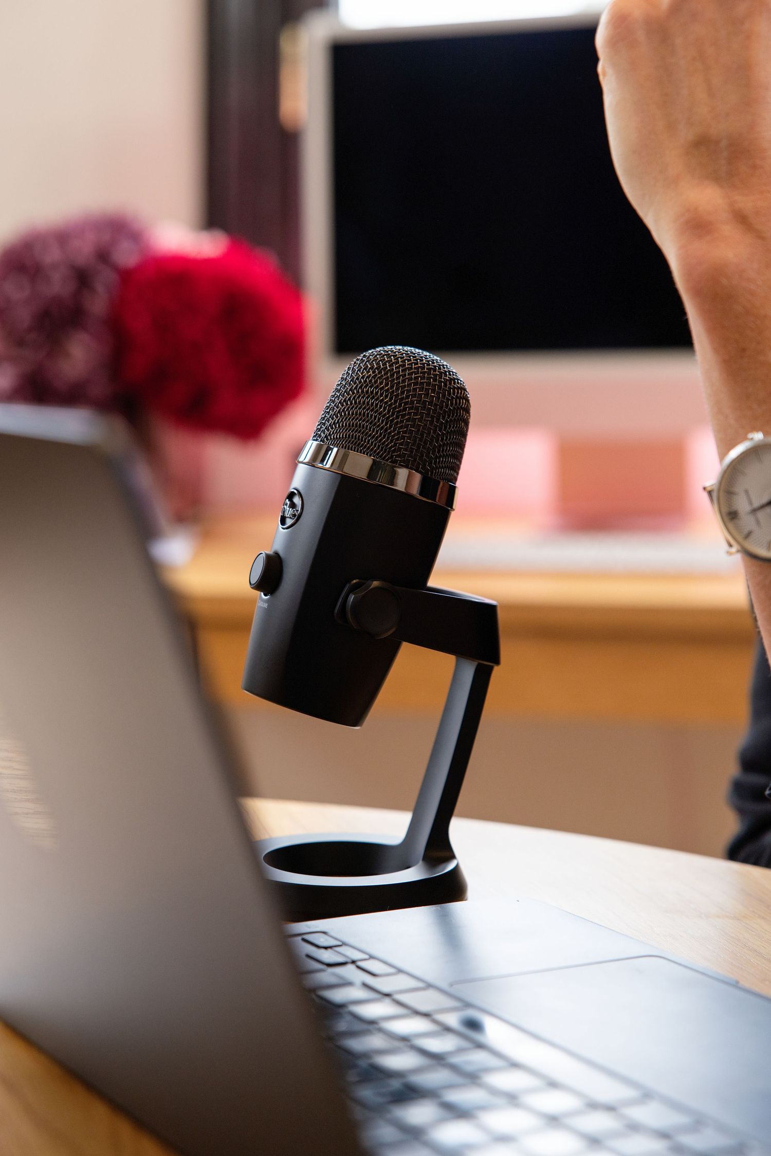 Black USB condenser microphone on desk beside laptop for podcast recording setup.