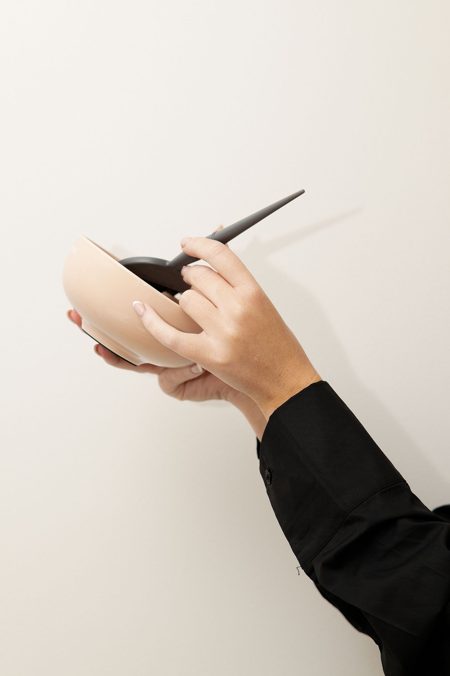 Hand holding a round pink object with a black stylus pen against a white background.
