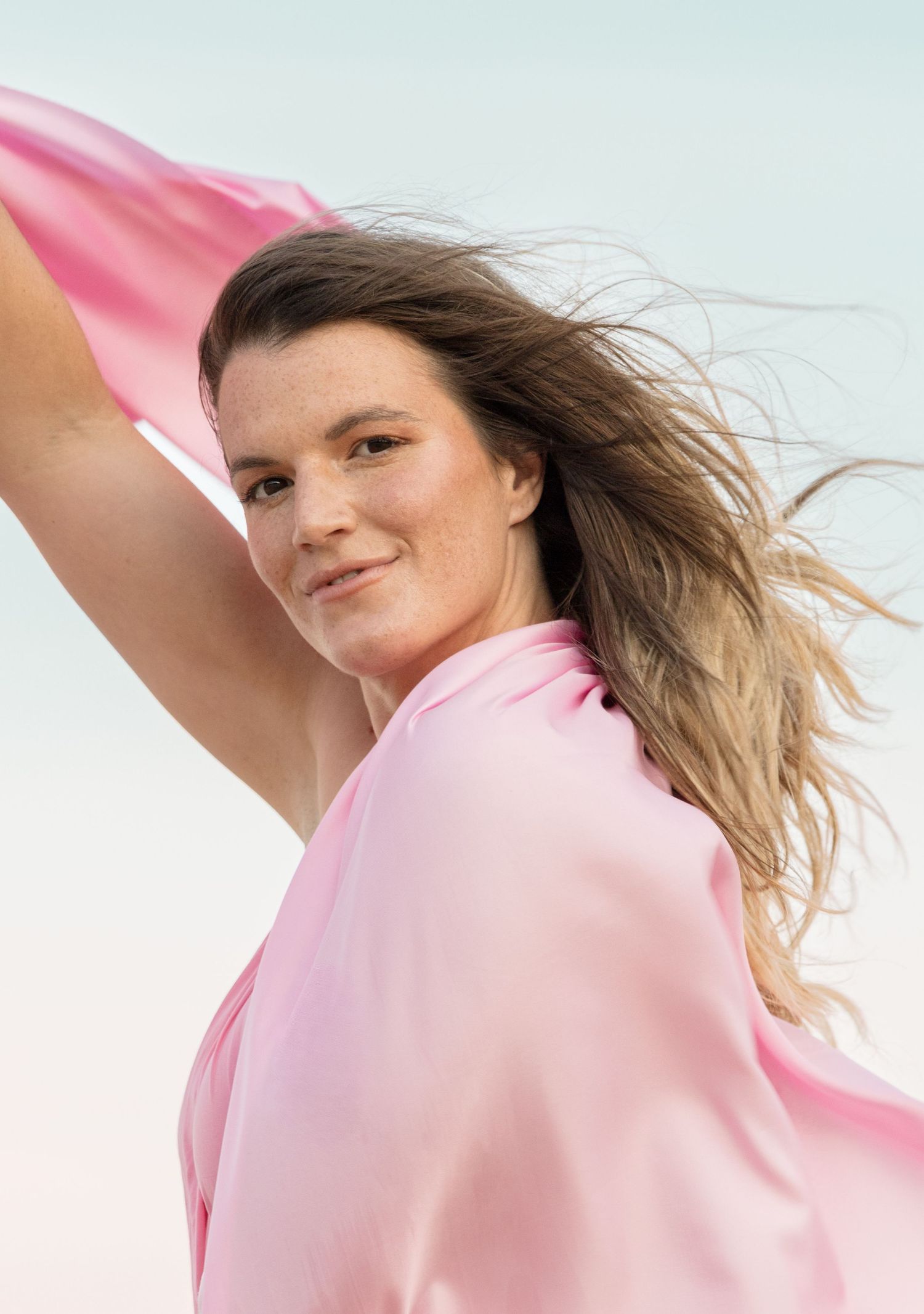 Person in pink shirt with windswept hair poses dynamically against light background in creative fashion portrait series.