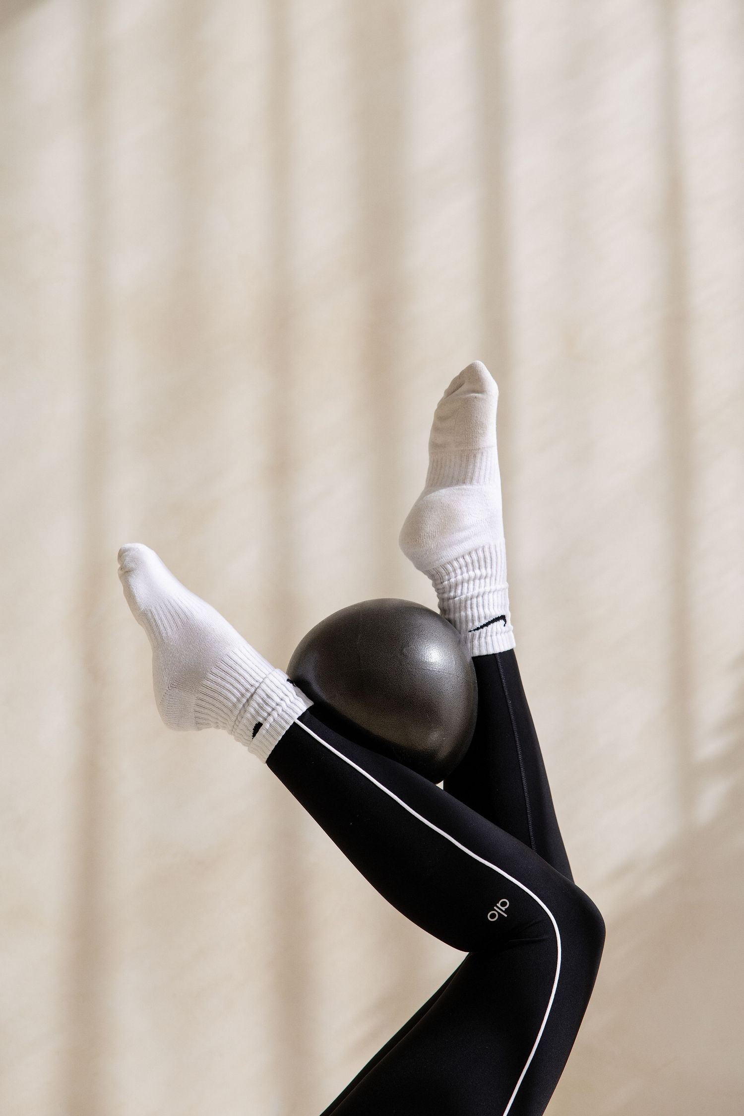 Legs wearing black piped leggings and white socks raised in the air with a pilates ball between them.