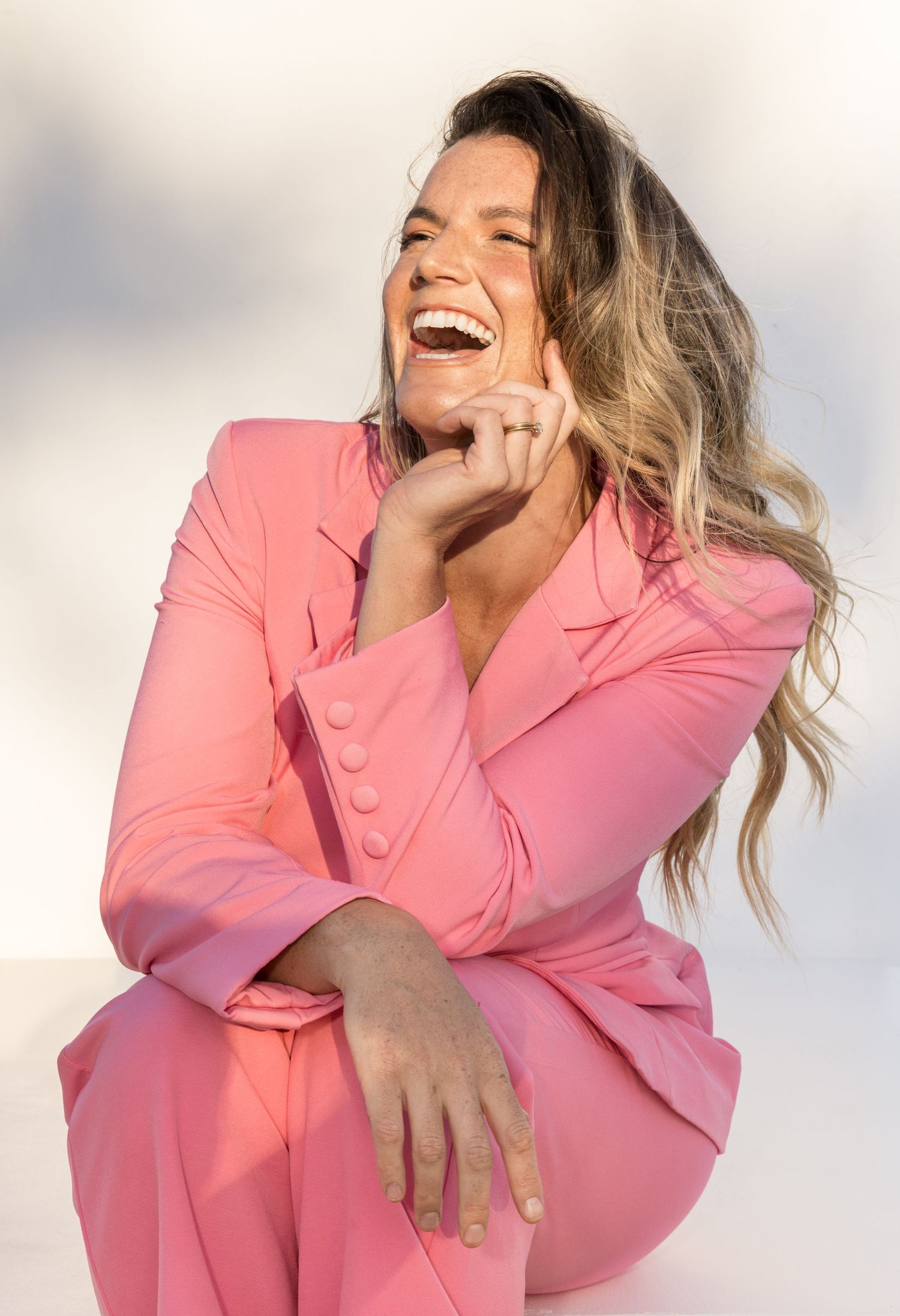Person in pink blazer laughing joyfully against white background in artistic portrait series.