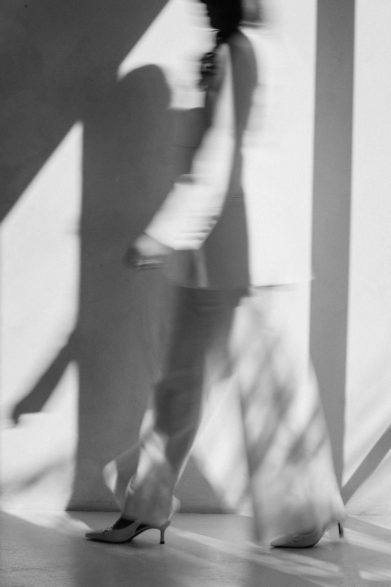 Black and white motion blur photo of woman walking in white suit and heels.